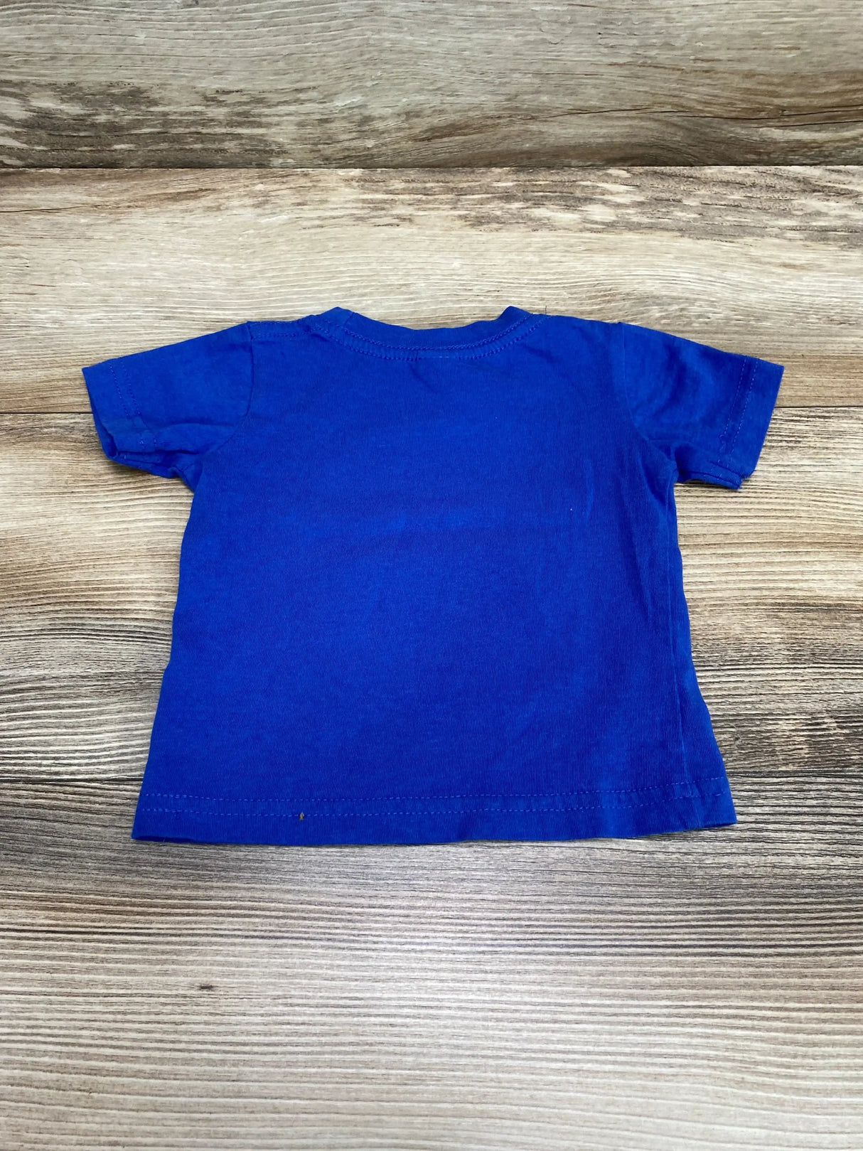 Back view of Cotton Heritage King of the Sea blue short-sleeve 6M toddler shirt on wood background with small spot near hem
