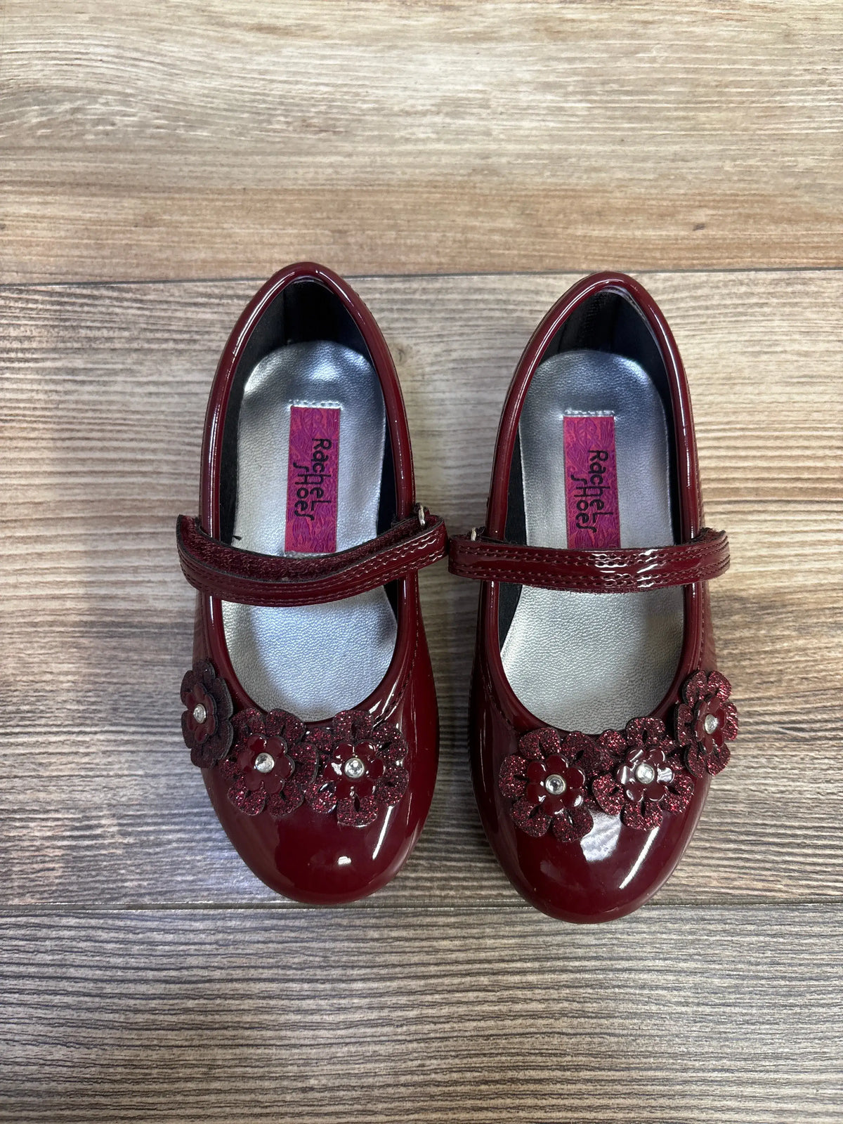 Top view of Rachel Shoes Lil Abelina flats showing glossy burgundy patent leather, floral vamp accents, and halo straps