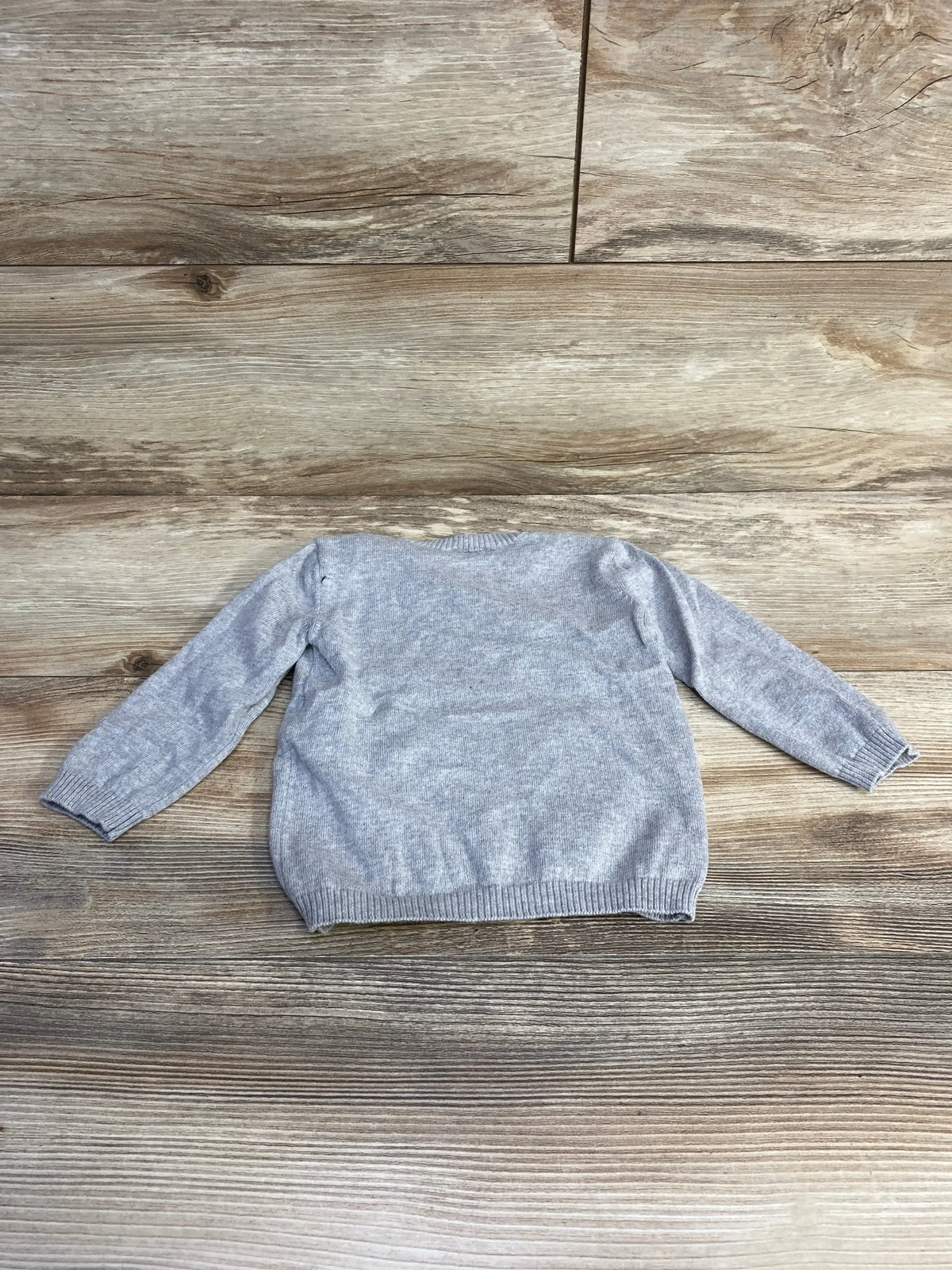 Back view of United Colors of Benetton grey rabbit baby sweater (9-12 months) showcasing knit texture and ribbed cuffs and hem on wood background