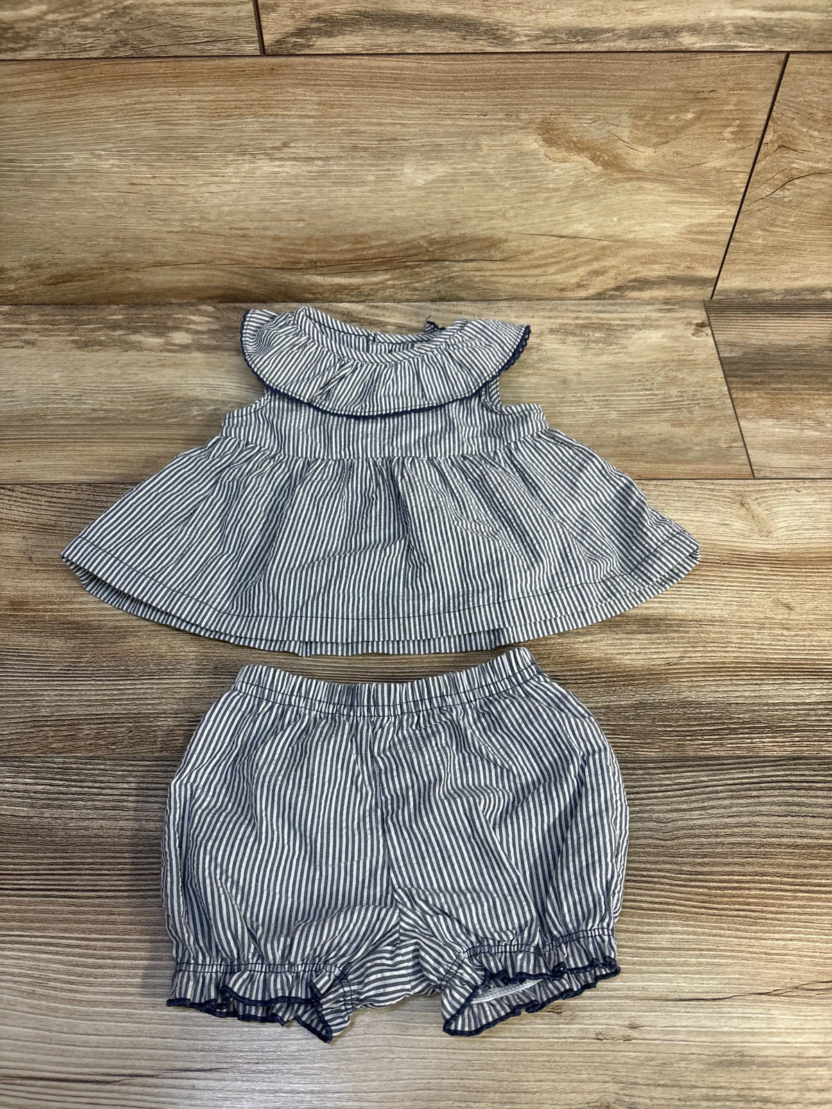 Flat lay of Just One You striped top and bloomers set showcasing blue stripes and ruffled trim on a wood-grain background