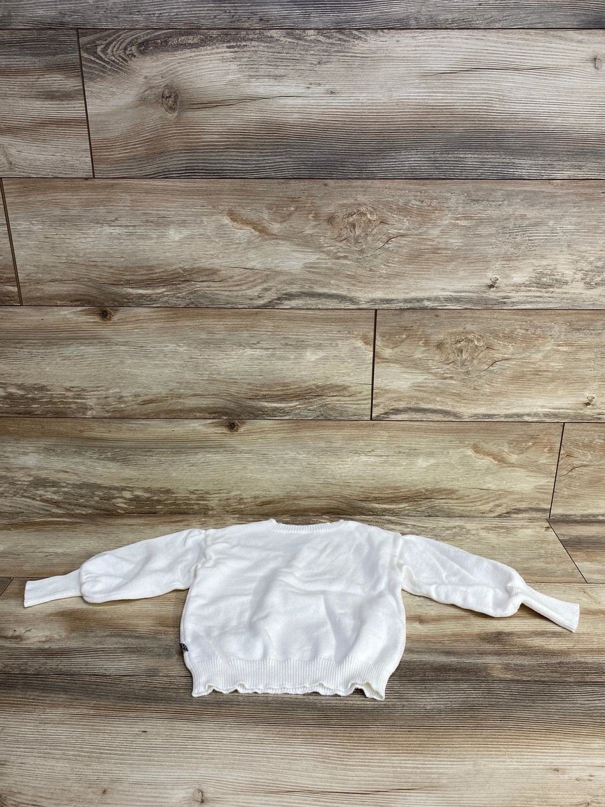 White long-sleeve toddler sweater laid flat on wood plank flooring backdrop