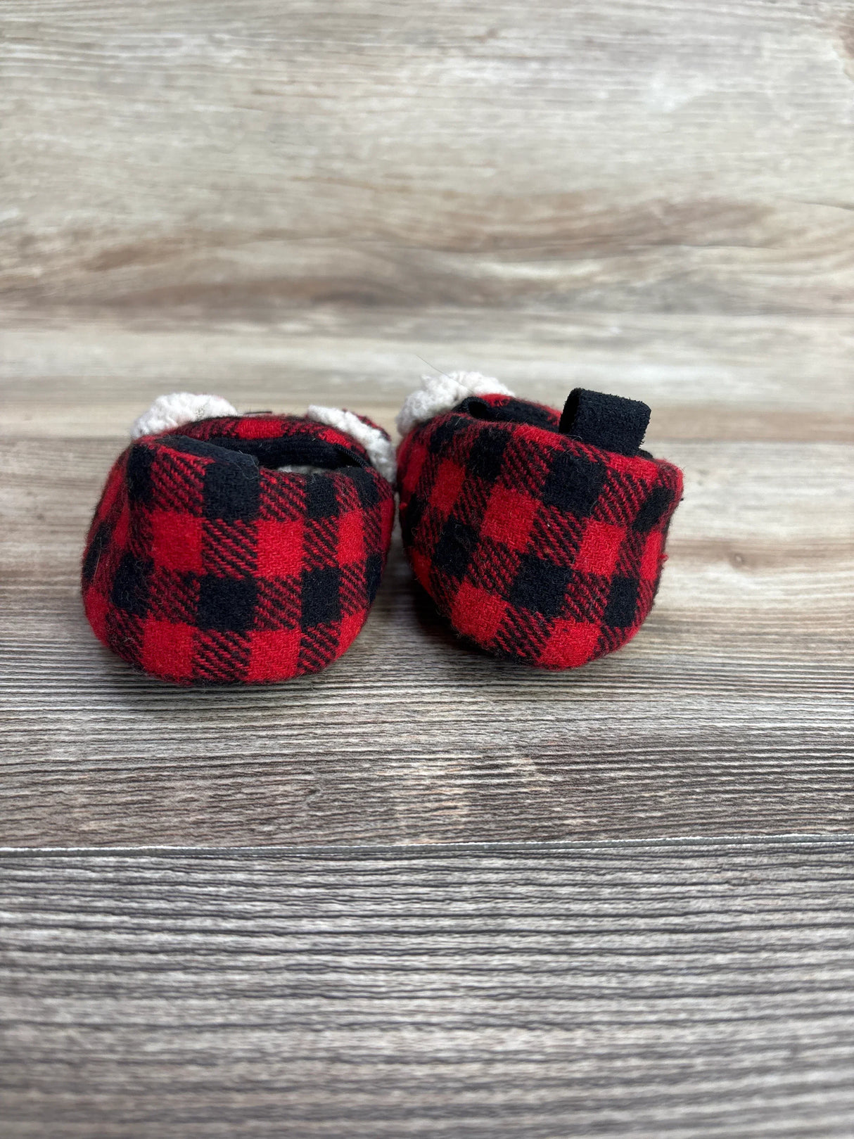Red and black plaid baby booties on wooden surface
