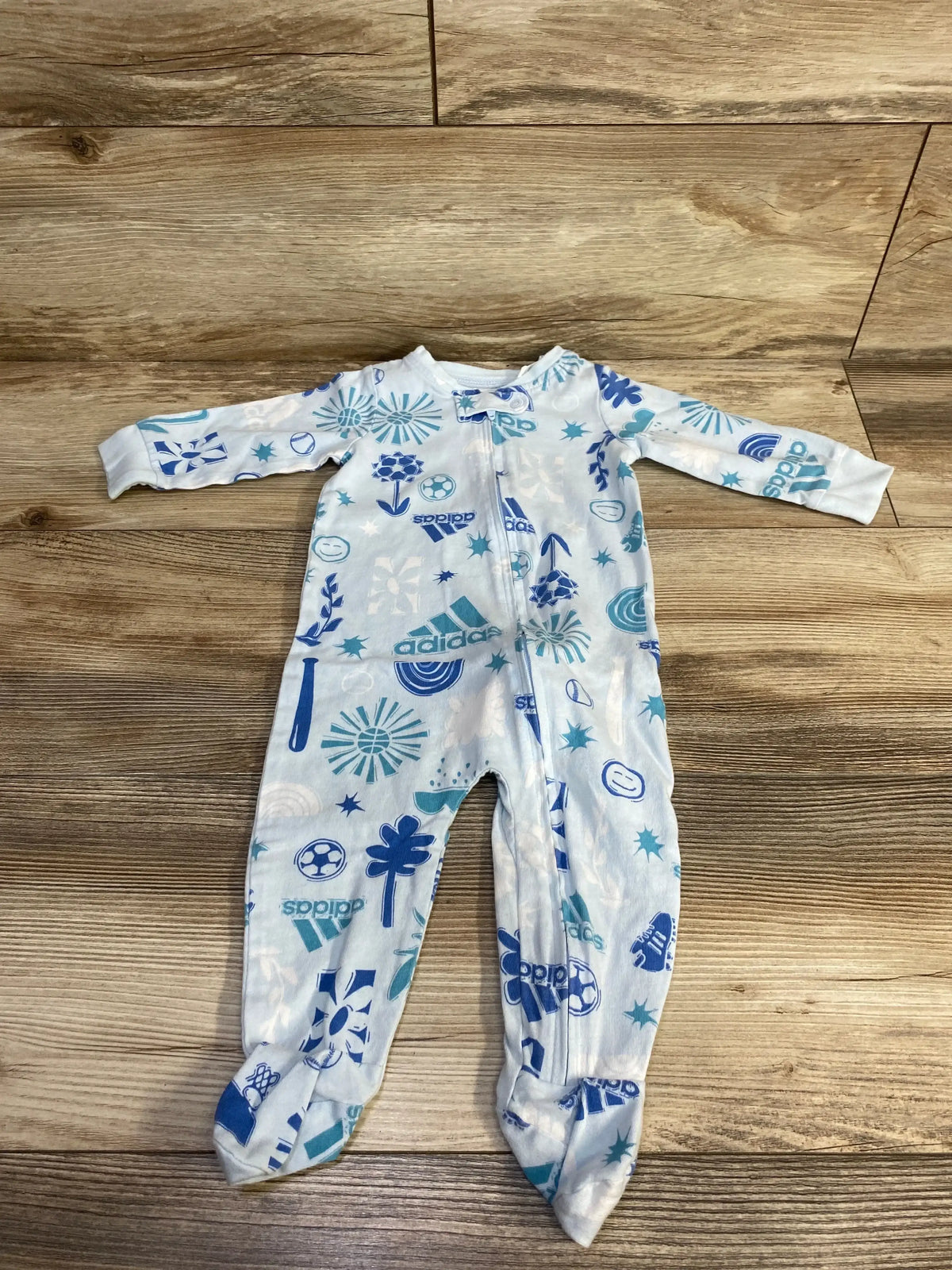 Flat lay of blue Adidas baby sleeper size 6m showing all-over sports logo print, front zipper and built-in feet on wood floor