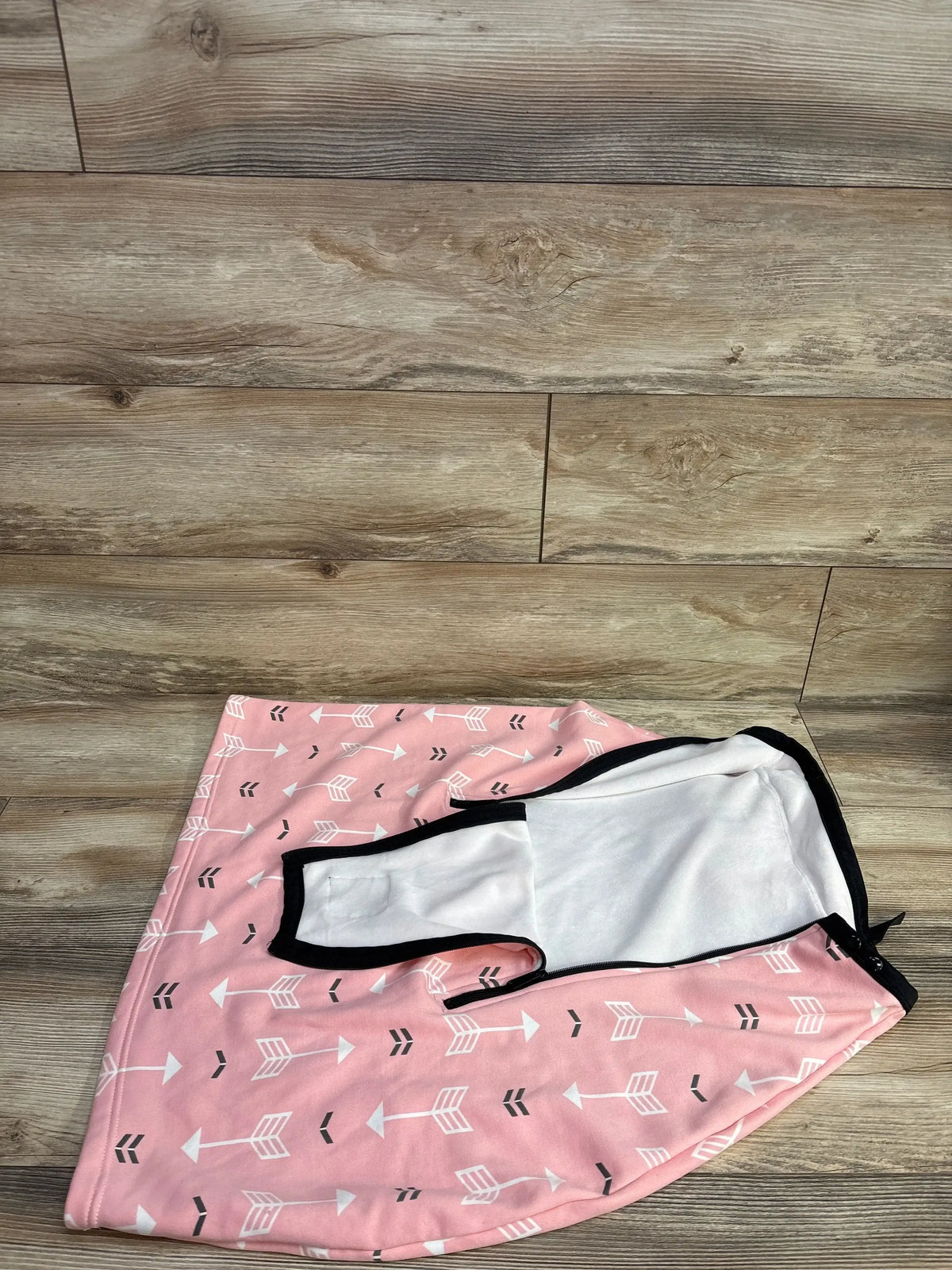Pink infant car seat cover with white arrow pattern on wood background
