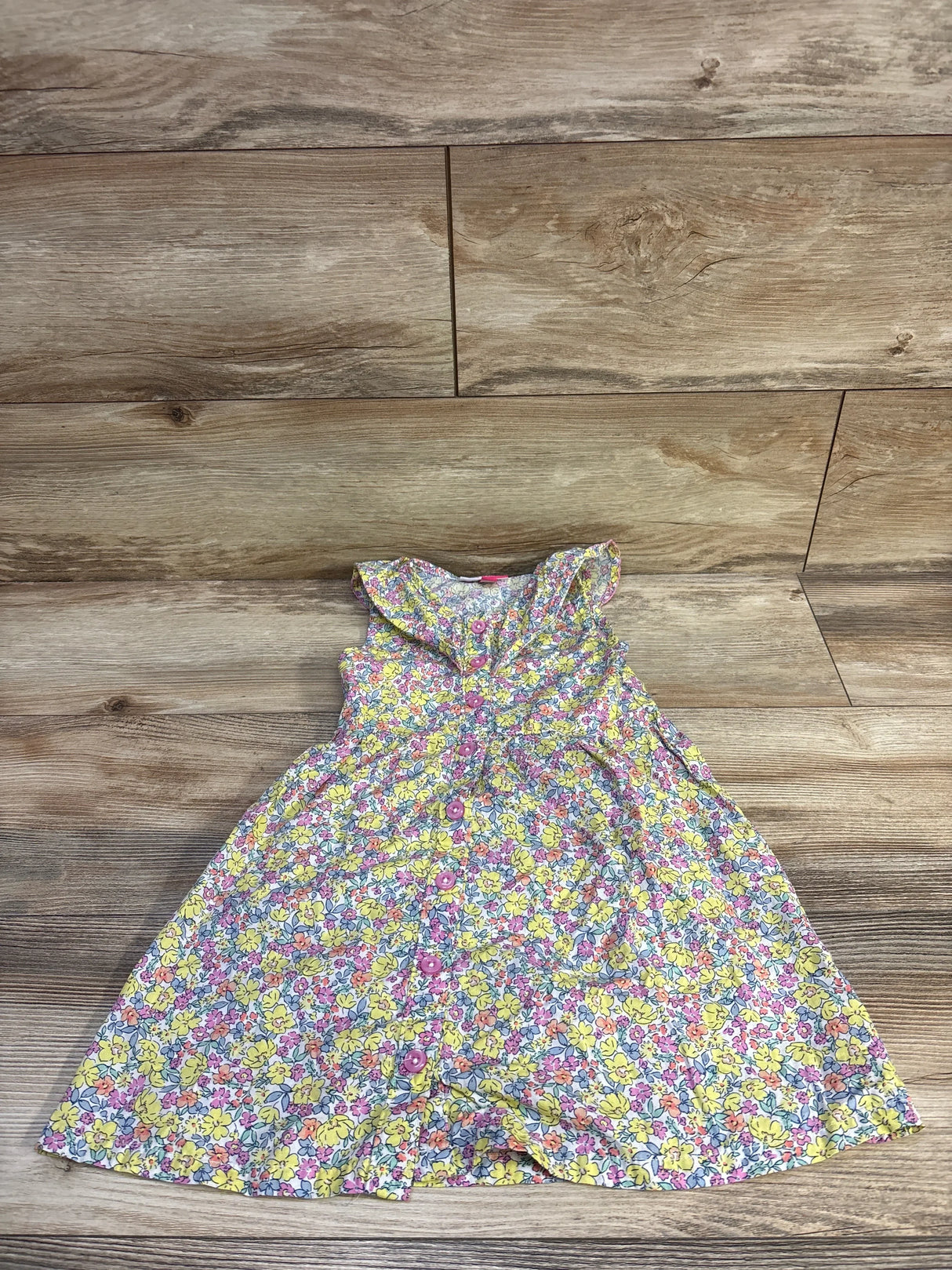 Top-down view of Penelope Mack girls yellow floral button-front dress showcasing ruffled collar and front buttons on wood floor