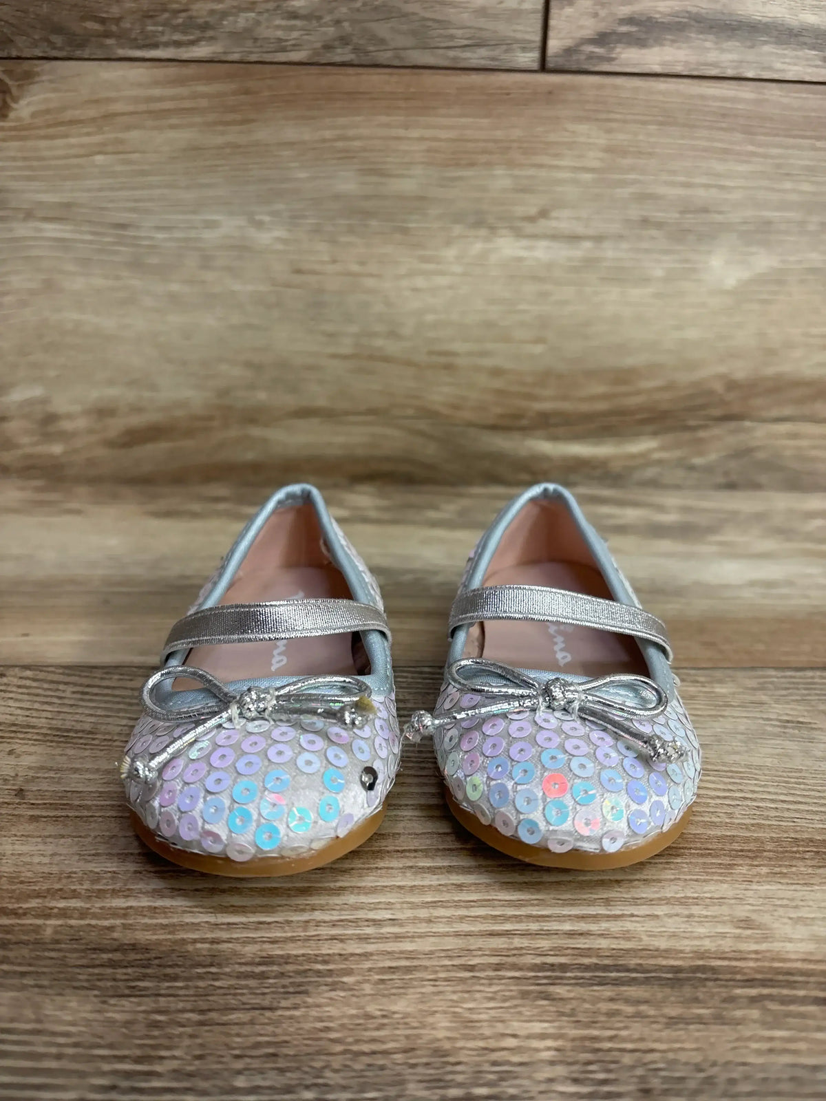 Pair of toddler girls' silver sequin Mary Jane shoes with bows on wooden floor