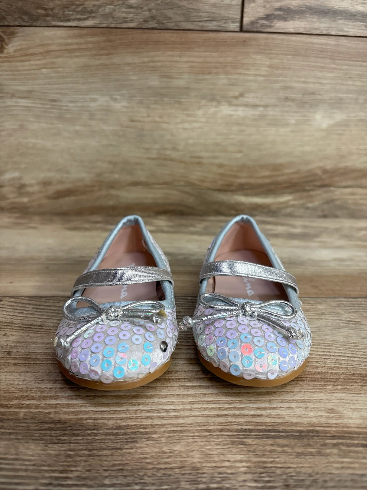 Pair of toddler girls' silver sequin Mary Jane shoes with bows on wooden floor