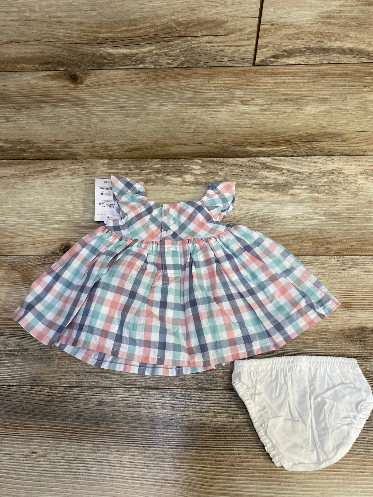 Flat lay of newborn plaid dress with ruffle cap sleeves and matching white bloomers on wood background