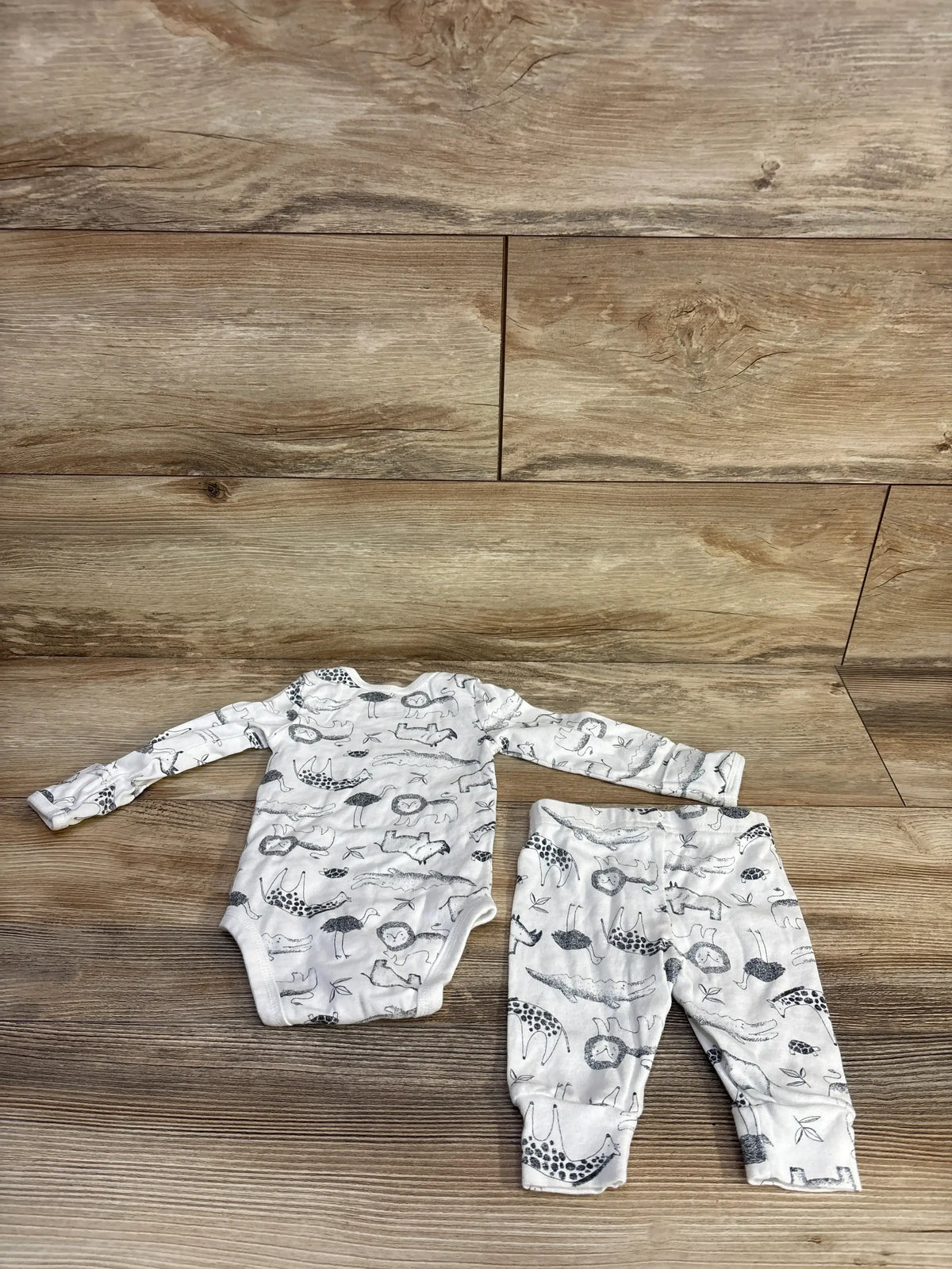 Top-down view of white 2-piece baby bodysuit and pants set size 3M featuring gray animal sketches on wood floor background