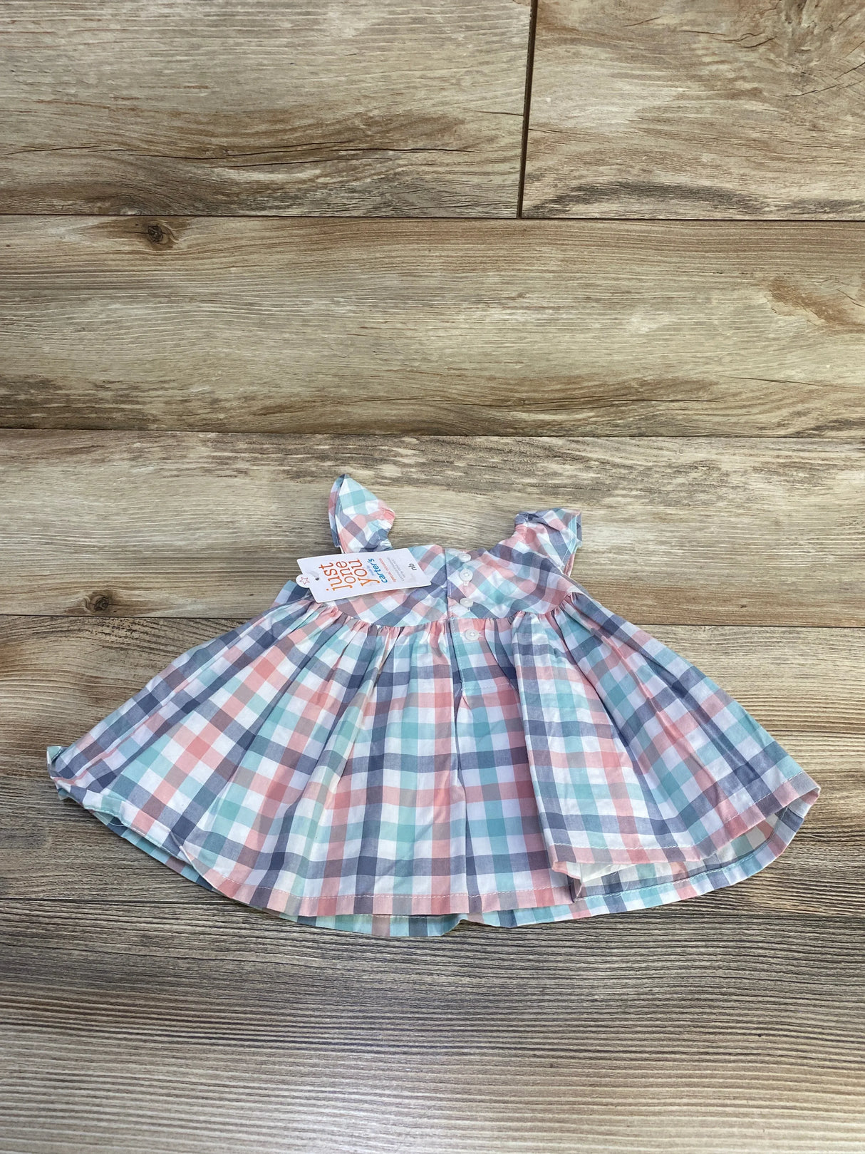 Top-down view of newborn plaid dress with pastel checks, ruffle sleeves and front buttons on wood background