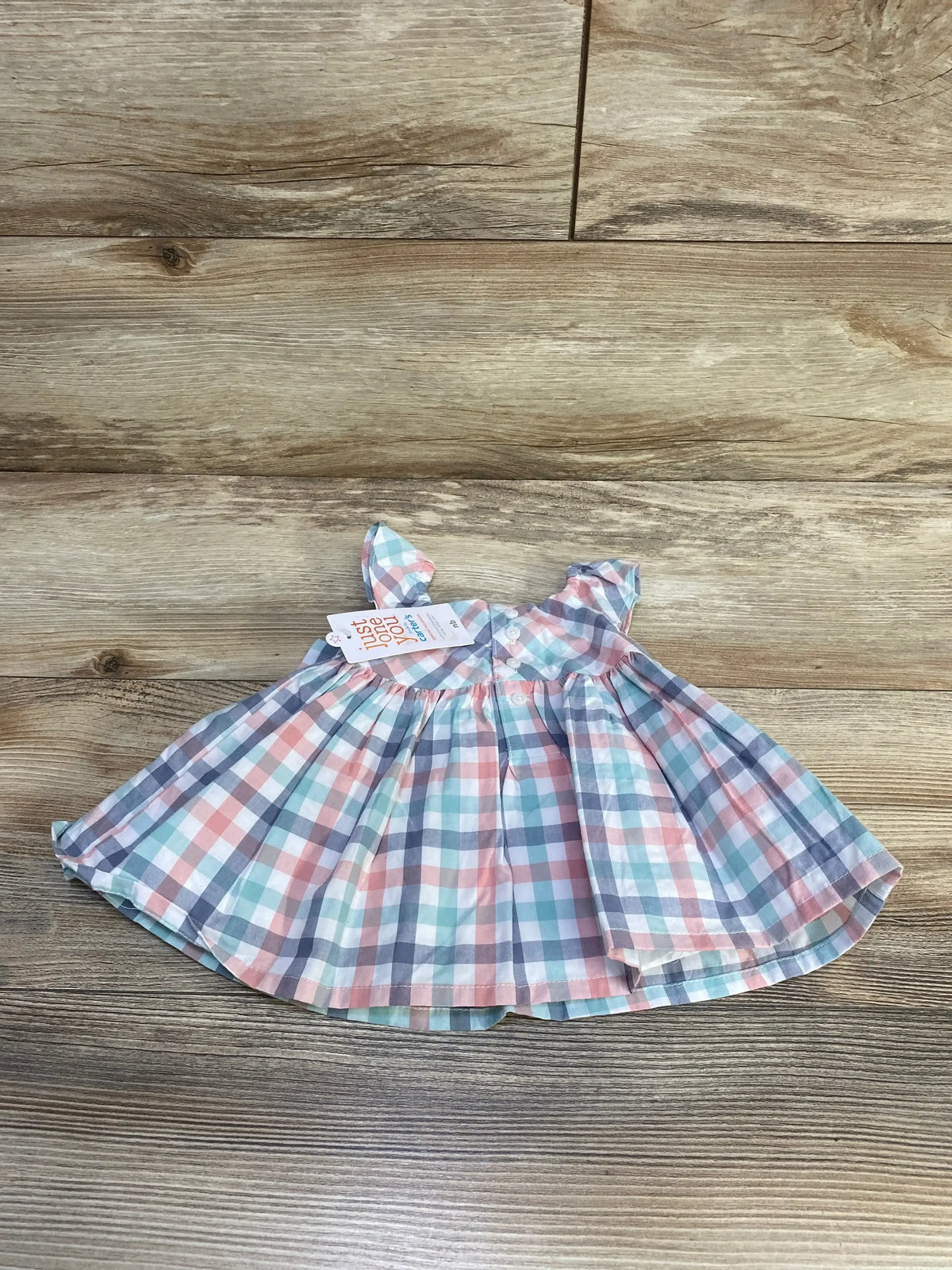 Top-down view of newborn plaid dress with pastel checks, ruffle sleeves and front buttons on wood background