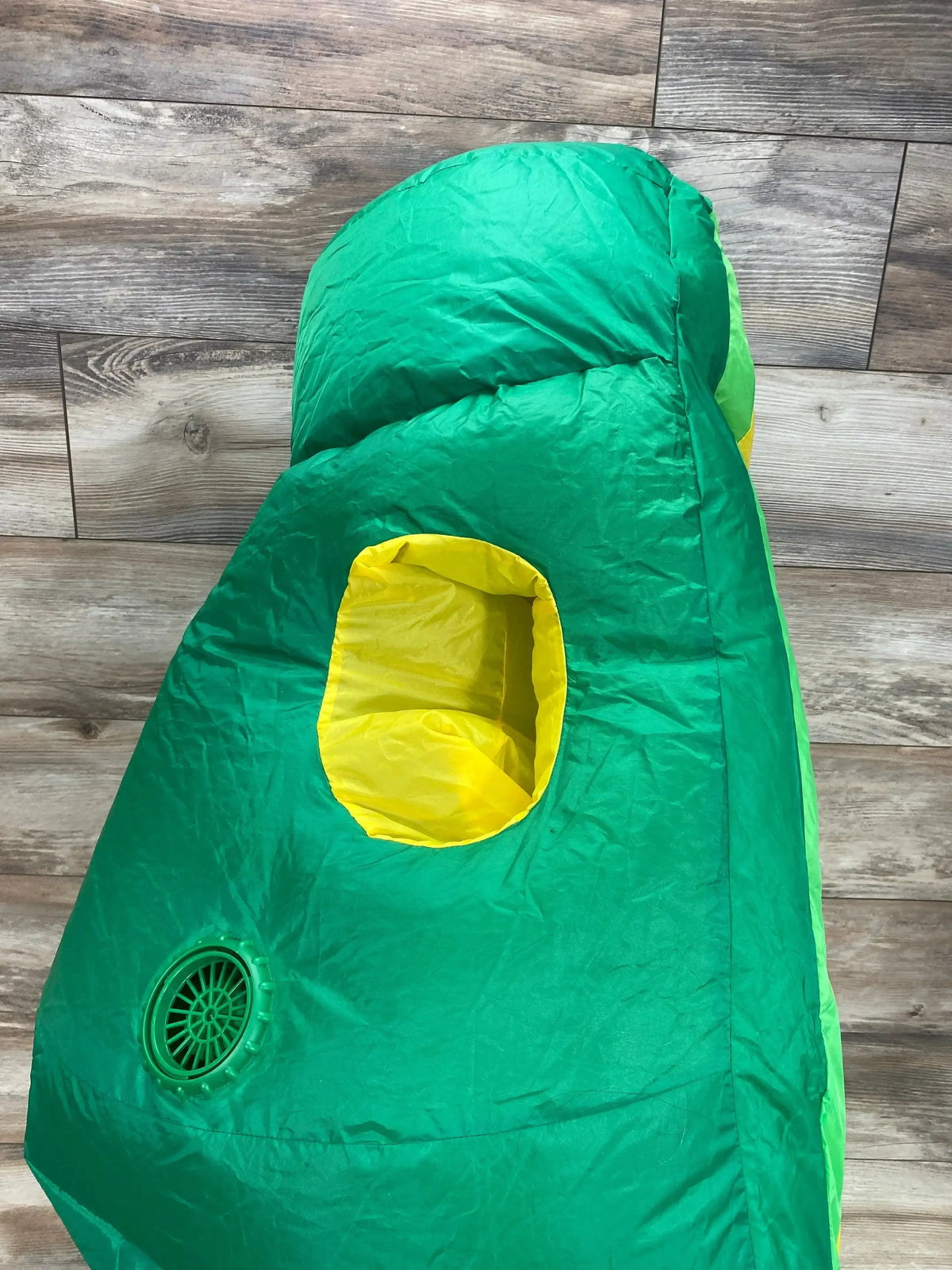 Front view of a green avocado inflatable costume showcasing a yellow pit opening and air fan with a wood plank background