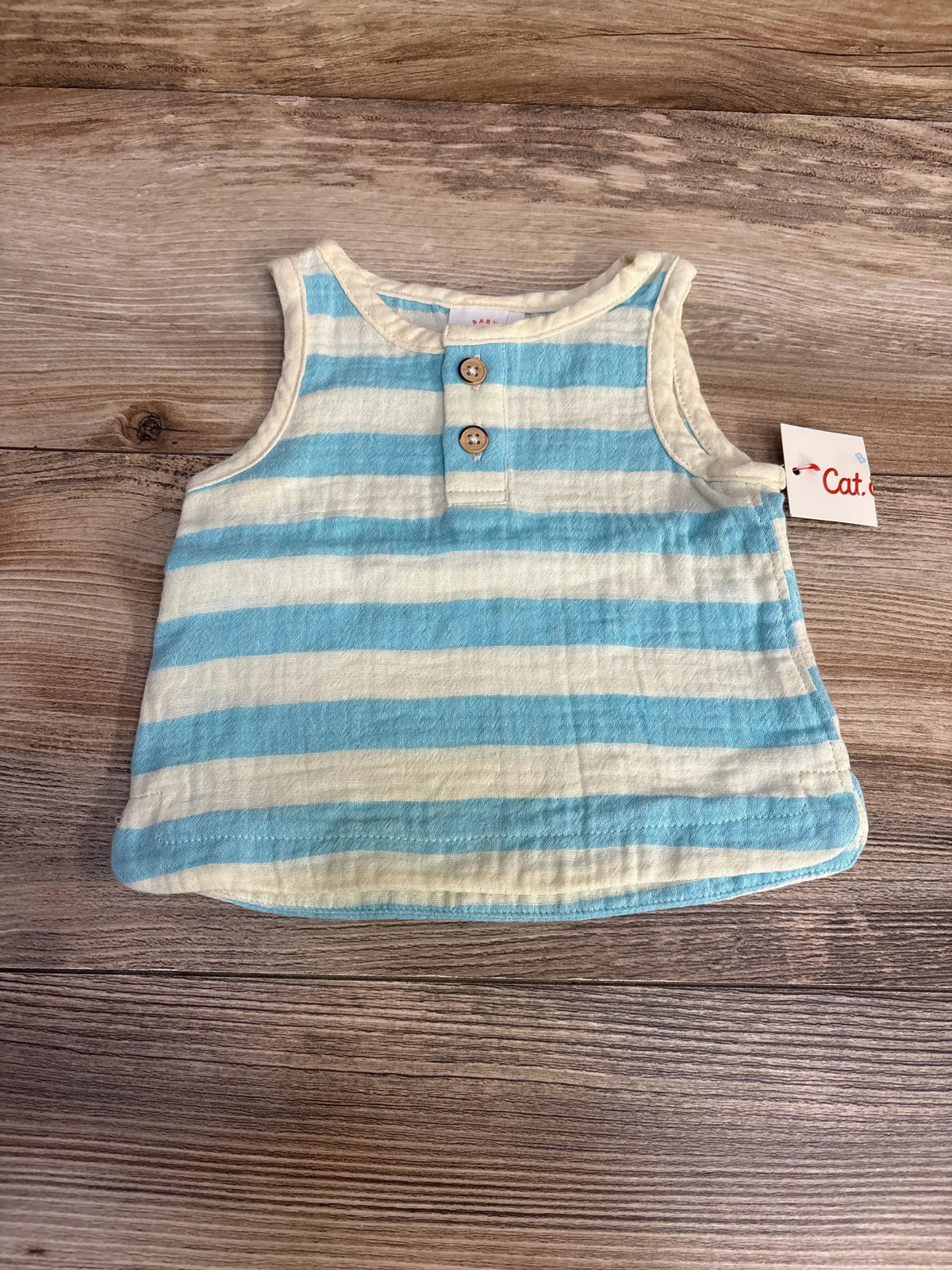 Flat lay of newborn striped tank top in blue and cream with two wood buttons, sleeveless, curved hem on wood background