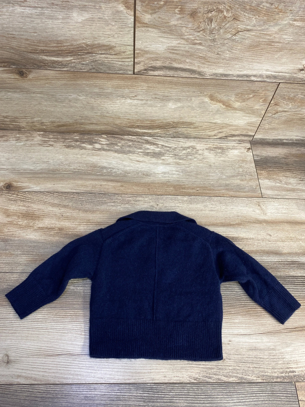 Navy blue long sleeve toddler sweater laid flat on wooden floor.