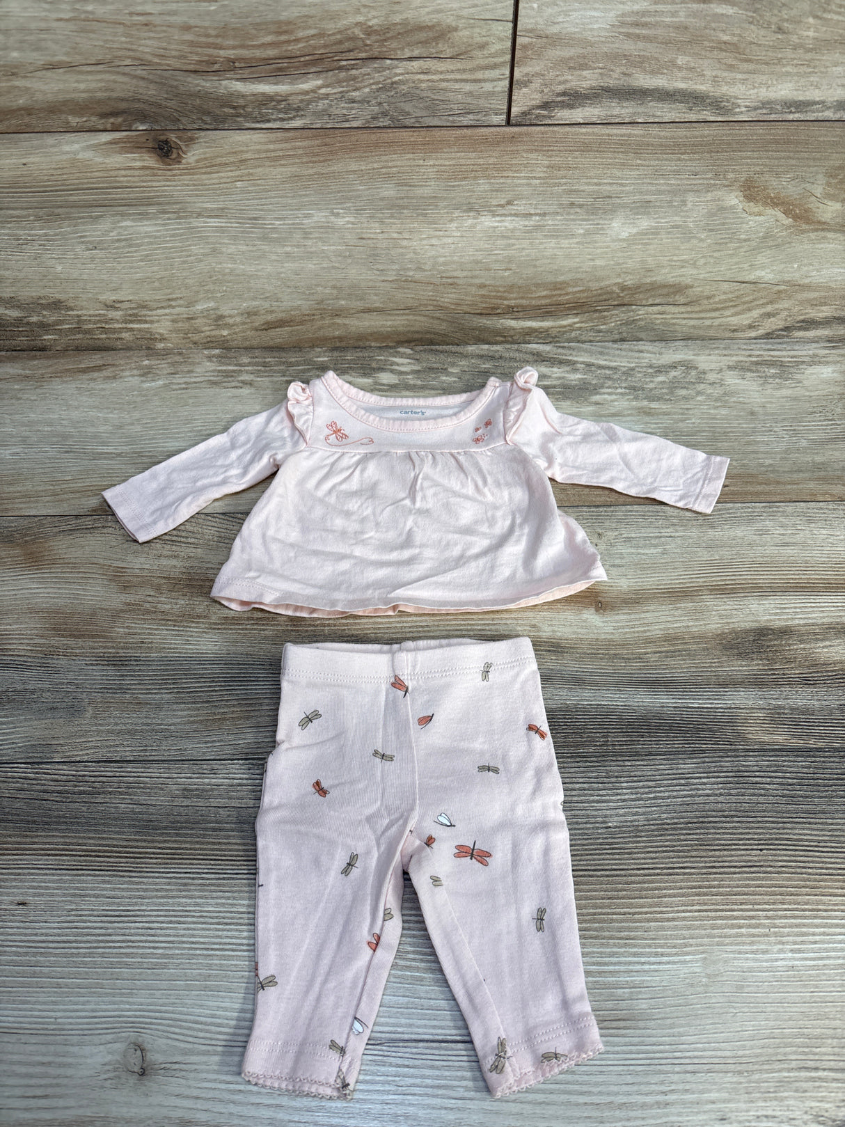 Pink baby outfit set with long-sleeve top and patterned pants on wood background