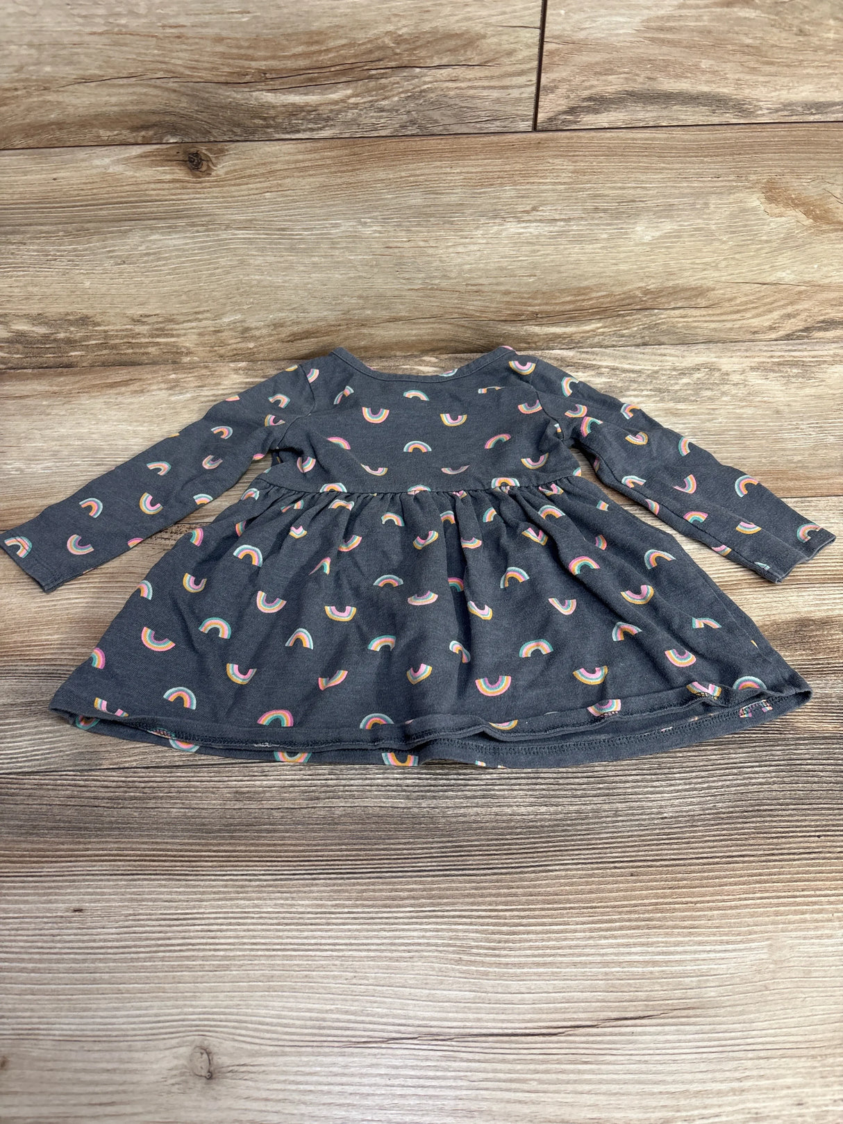 Dark gray long-sleeve toddler dress with colorful rainbow prints laid on wooden floor