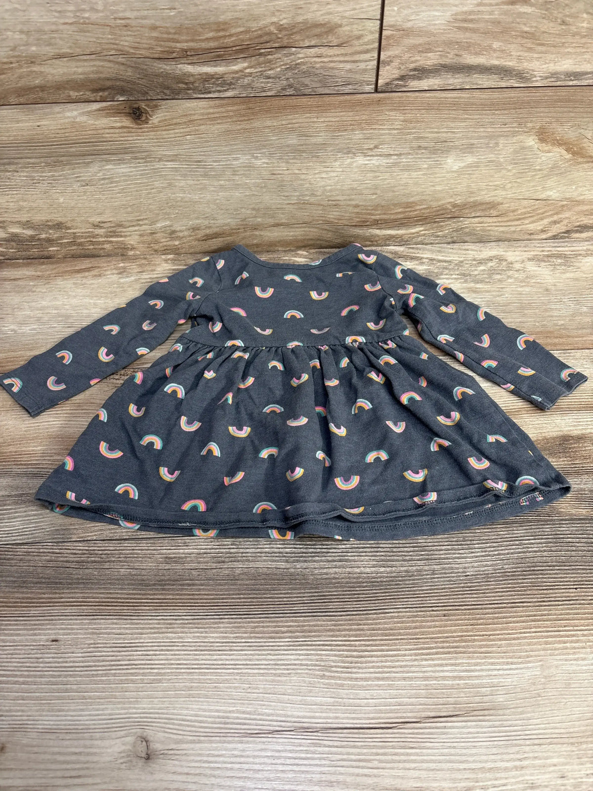 Dark gray long-sleeve toddler dress with colorful rainbow prints laid on wooden floor