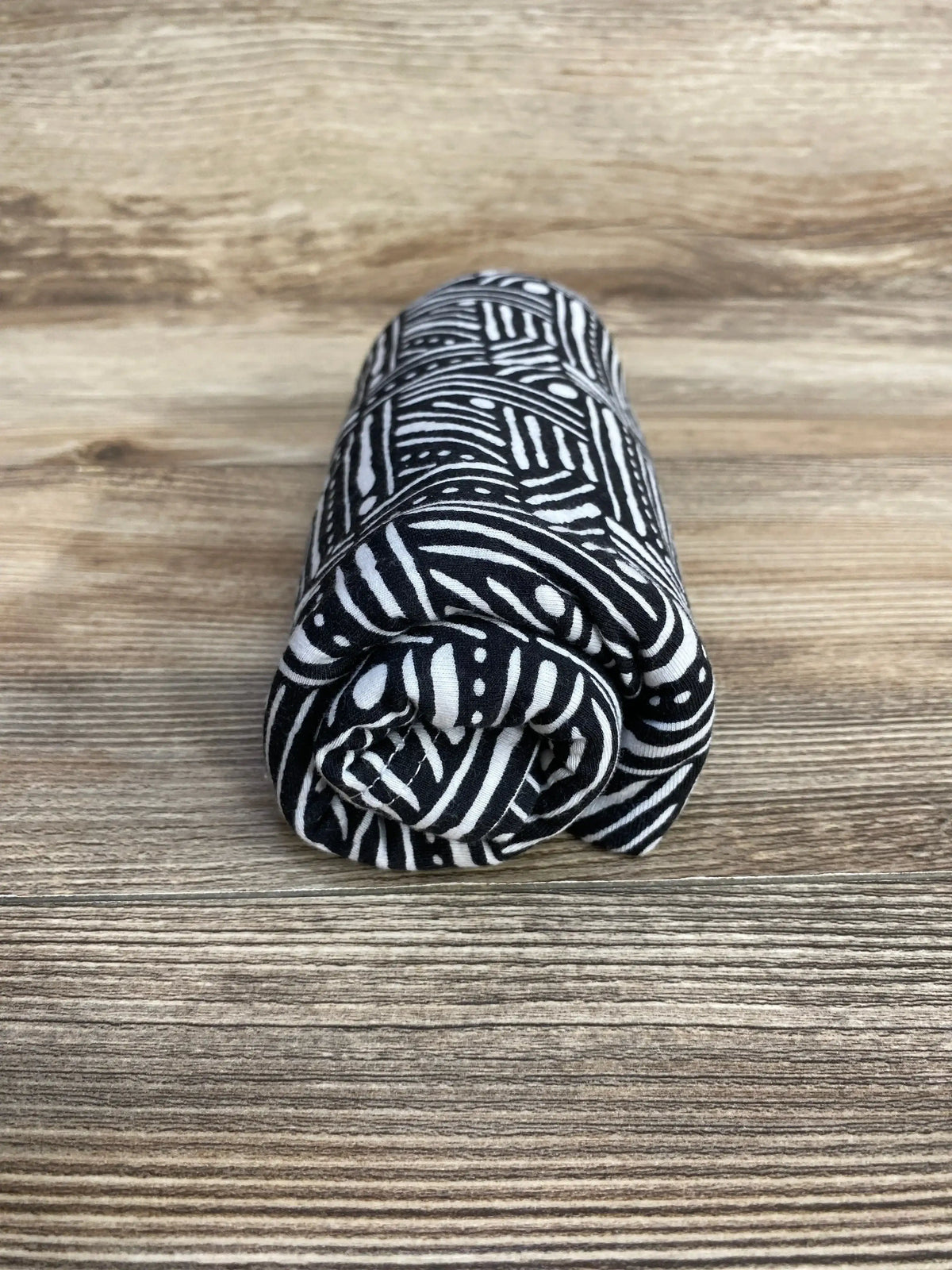 Front view of Trend Lab Geometric nursing cover rolled to show black-and-white geometric pattern on wood background
