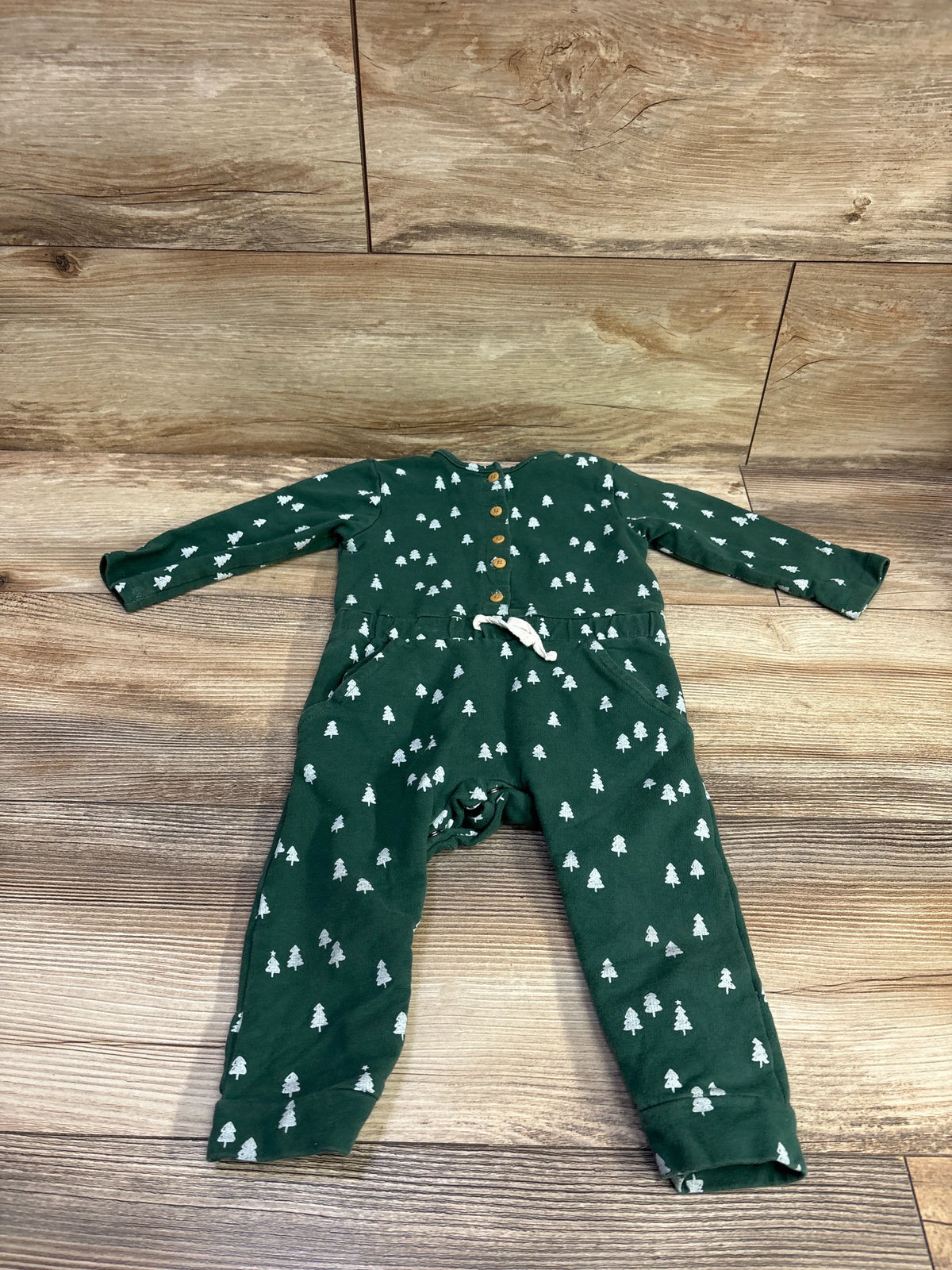 Top view of green Focus Kids Christmas Tree Coverall showcasing white tree print, button front, and drawstring waist on wood floor