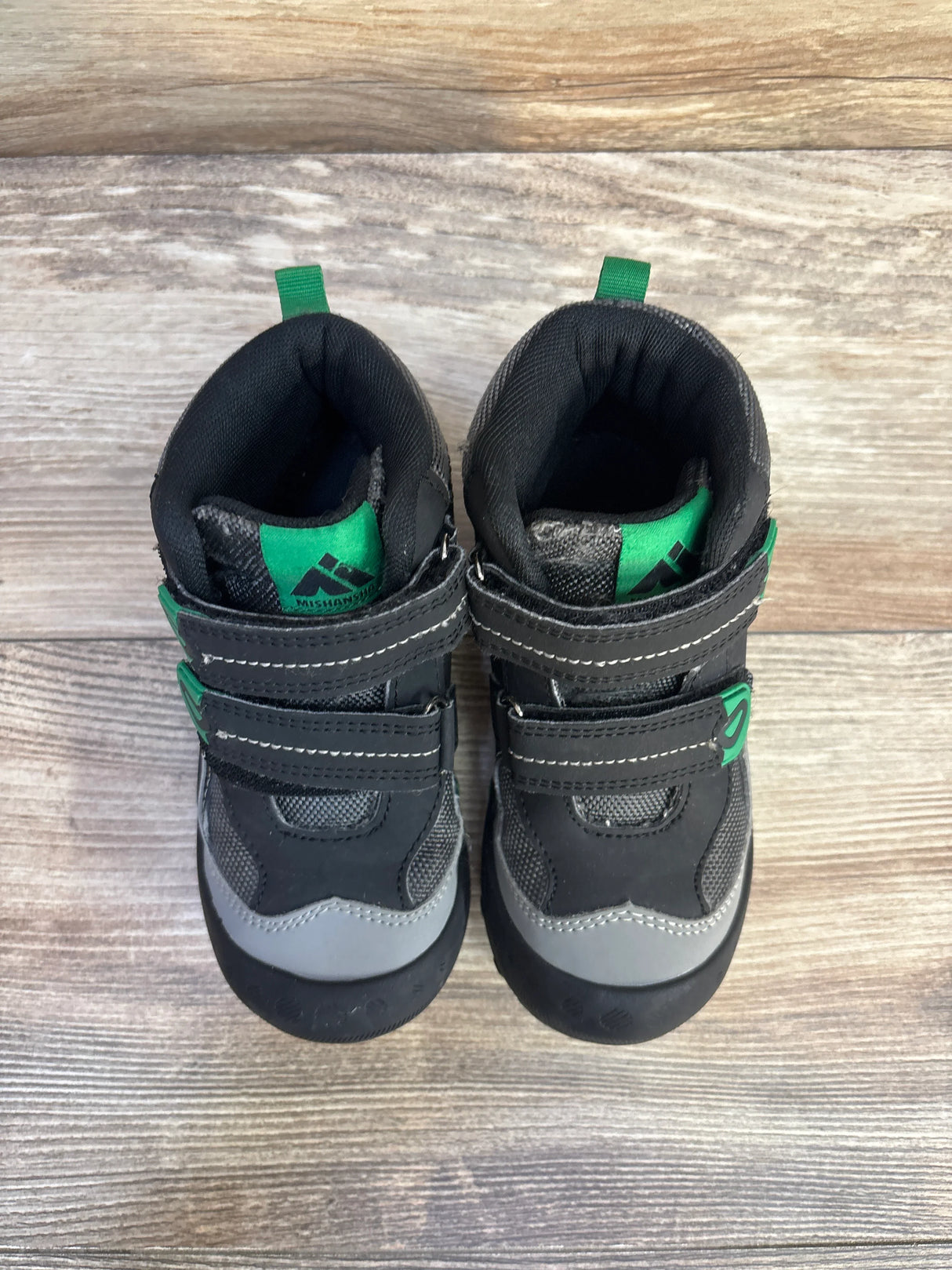 Pair of black and gray kids' sneakers with green accents on wooden floor