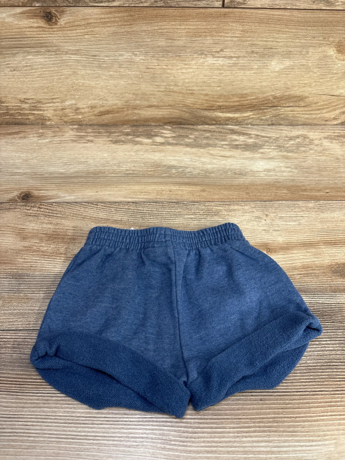 Flat lay of Tommy Hilfiger blue pull-on toddler shorts showcasing elastic waistband and rolled cuffs on wood background, size 2T
