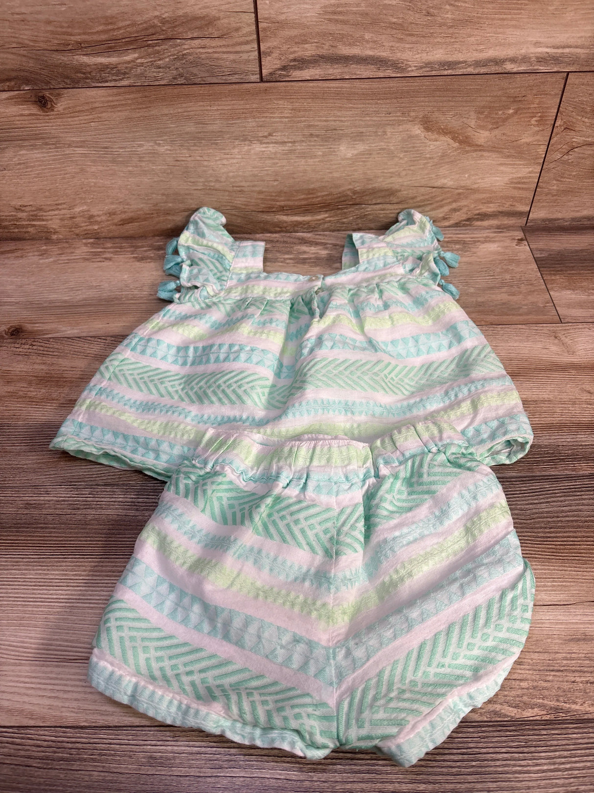 Flat-lay of toddler shabby chic 2-piece set with tassel sleeves and elastic-waist shorts, white with mint stripes on wood