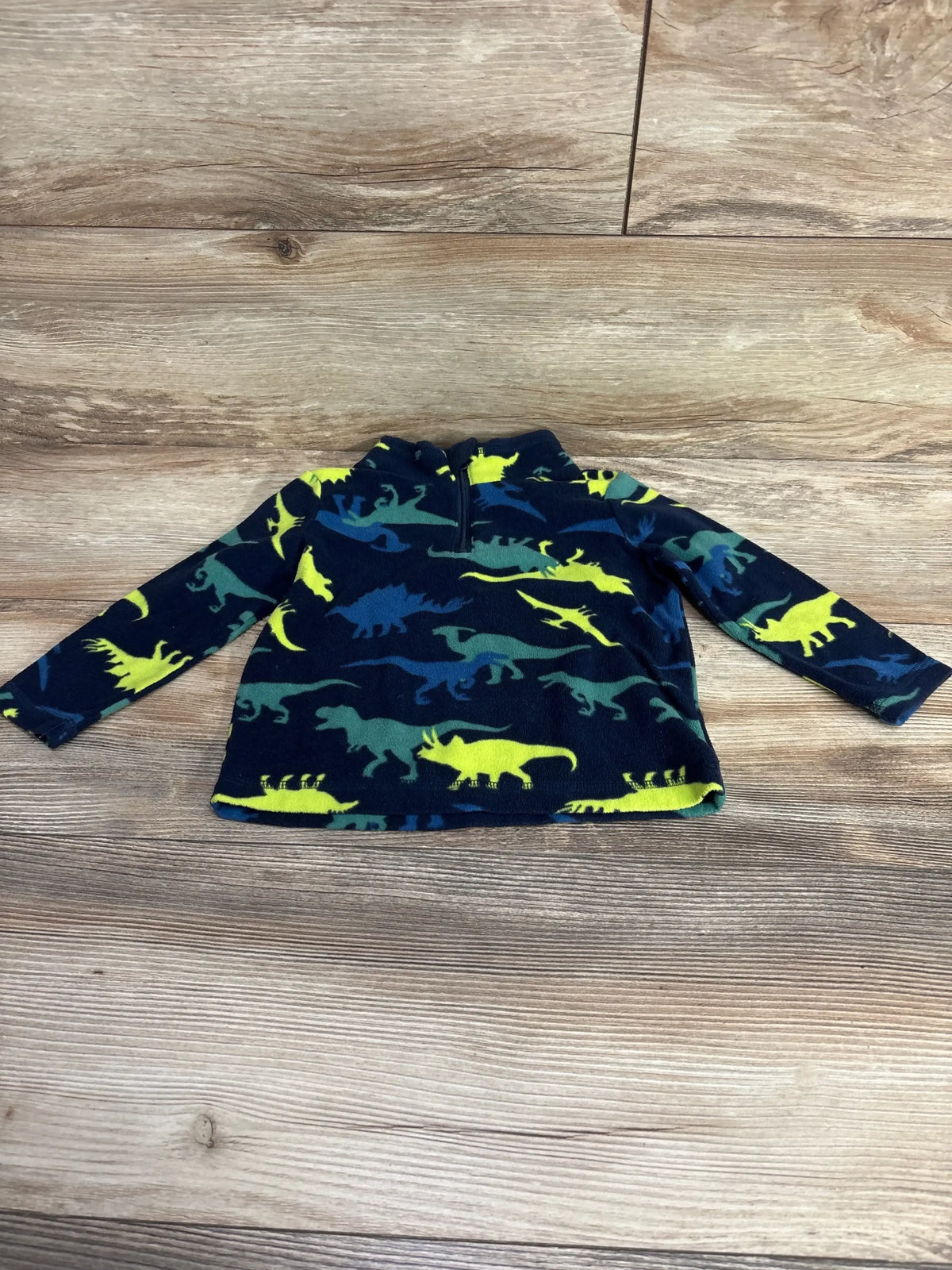 Children's navy blue fleece pullover with colorful dinosaur print and half-zip collar on wooden floor