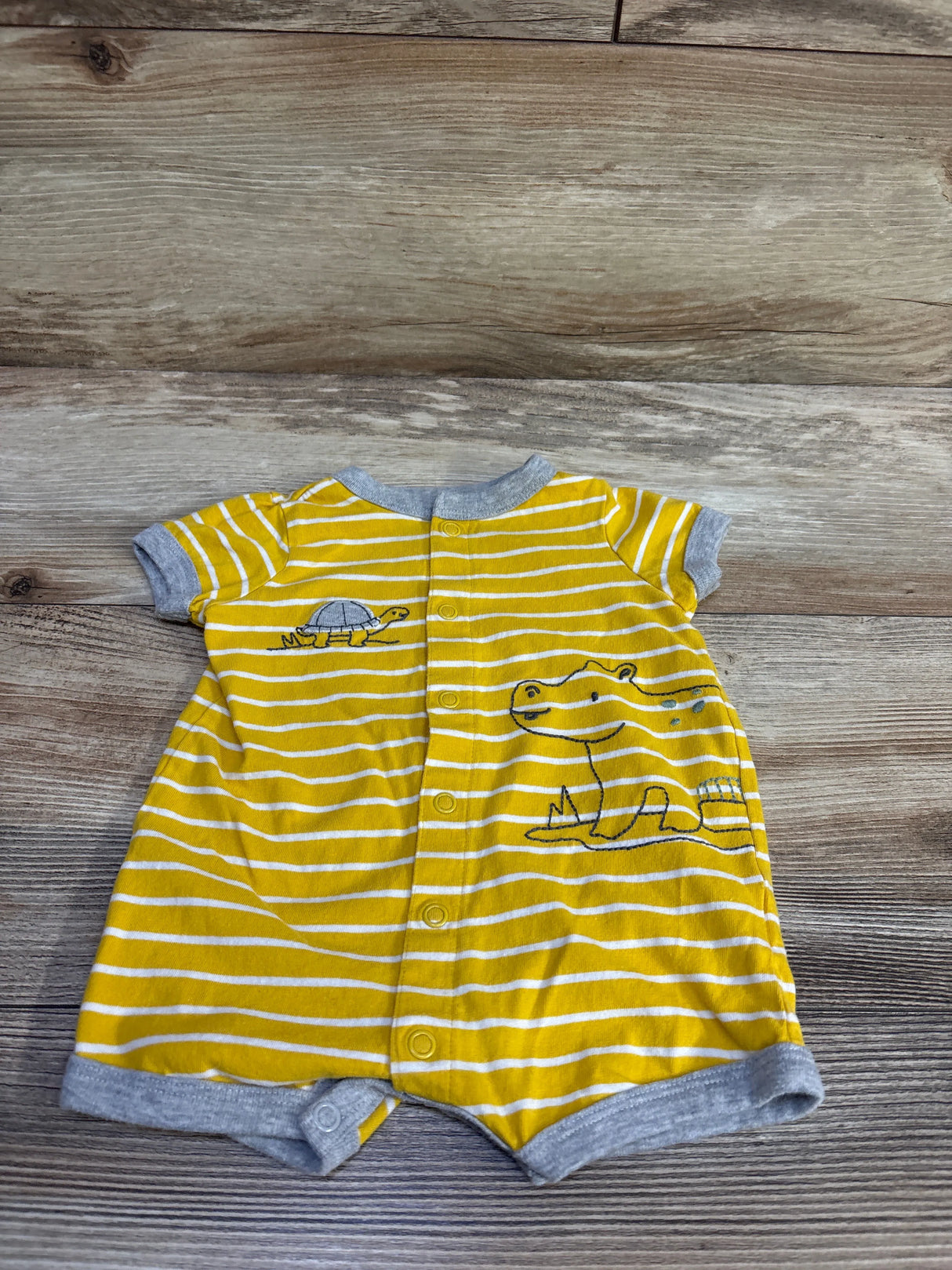 Flat lay of yellow striped Carter’s shortie romper with gray trim, button-front snaps and animal embroidery on wood background
