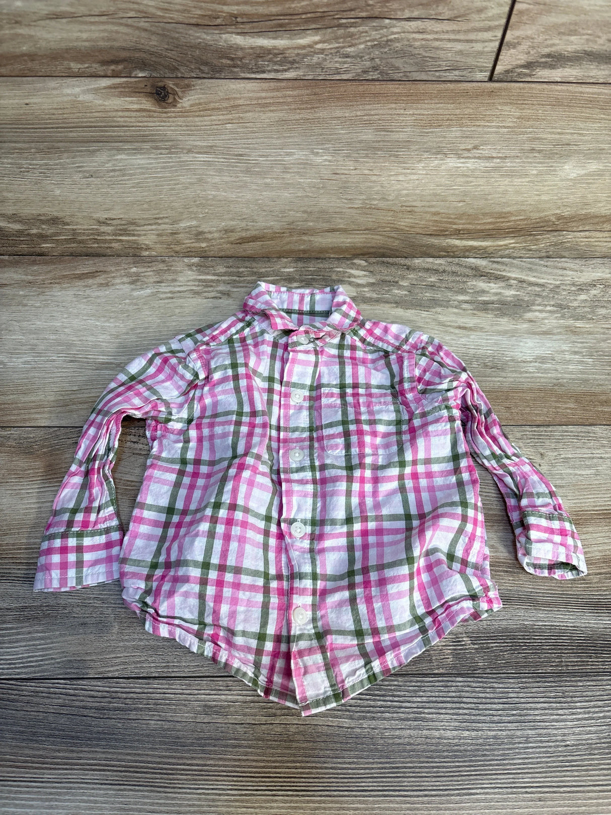 Pink and green plaid long sleeve button-up toddler shirt on wood background