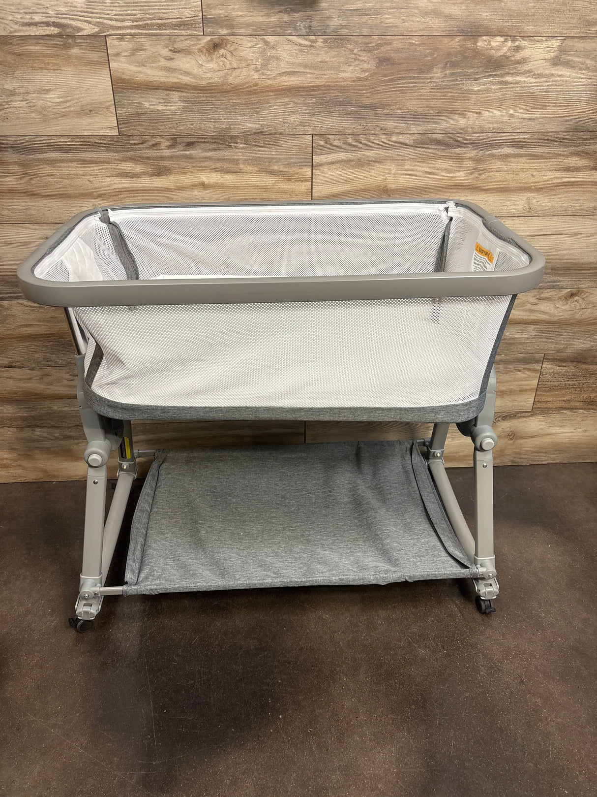 Gray mesh baby bassinet with storage shelf against wood wall, kids gear resale
