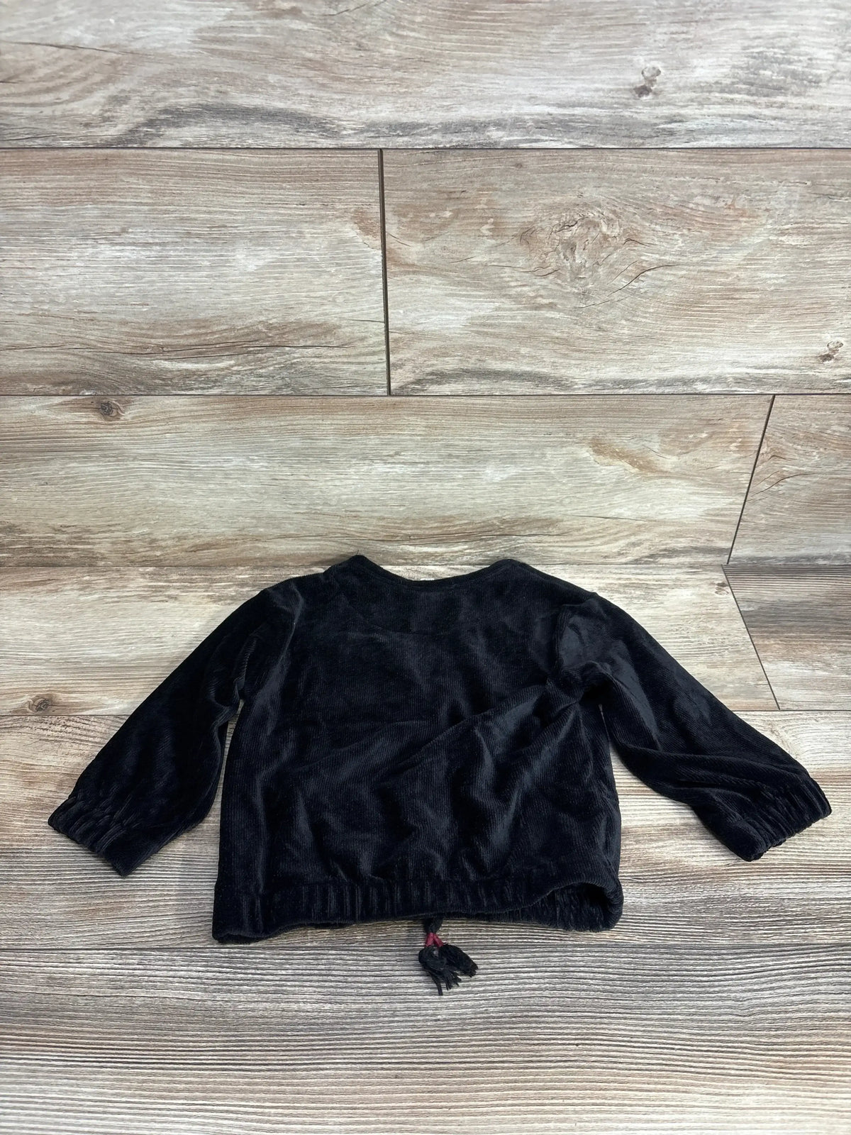 Black long sleeve toddler shirt with tassel detail on wood background