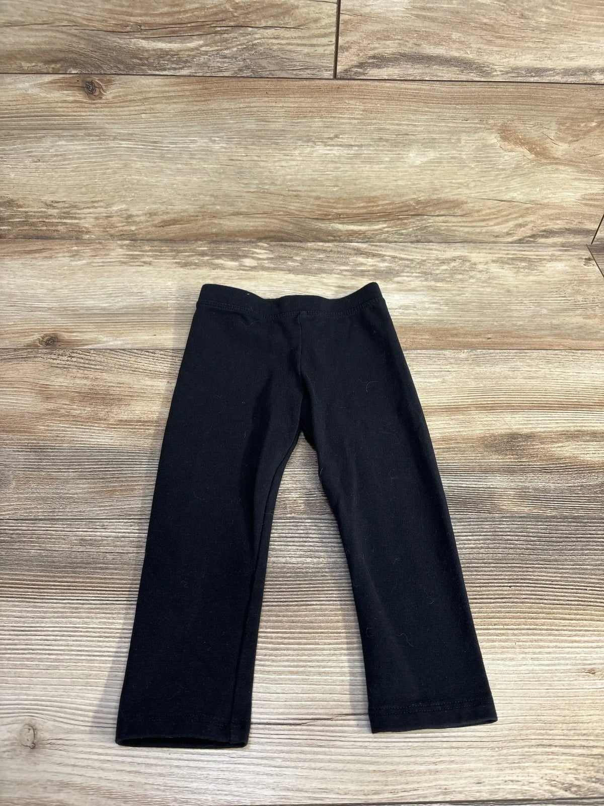 Flat lay of Amazon Essentials toddler black leggings showcasing elastic waistband and straight legs on light wood background