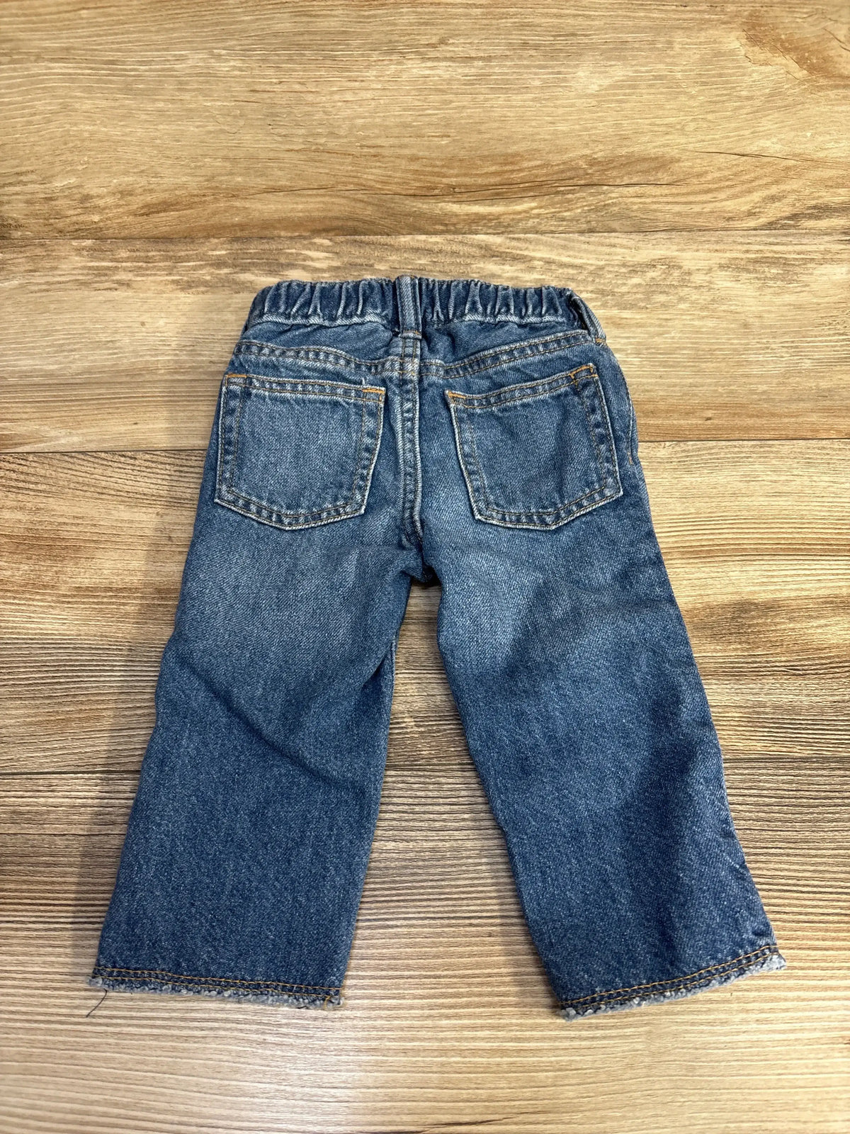 Back view of toddler blue denim jeans with elastic waistband on wood background