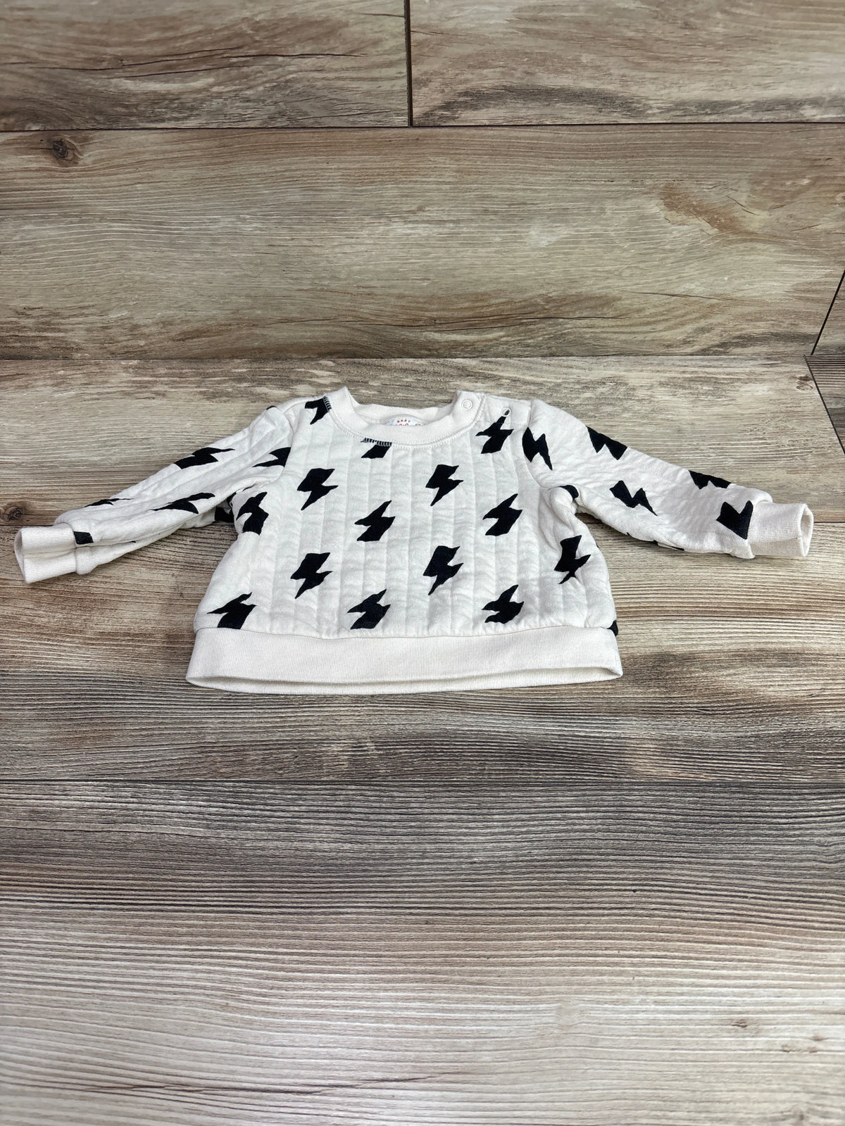 Ivory baby sweatshirt with black lightning bolt patterns on a wooden background