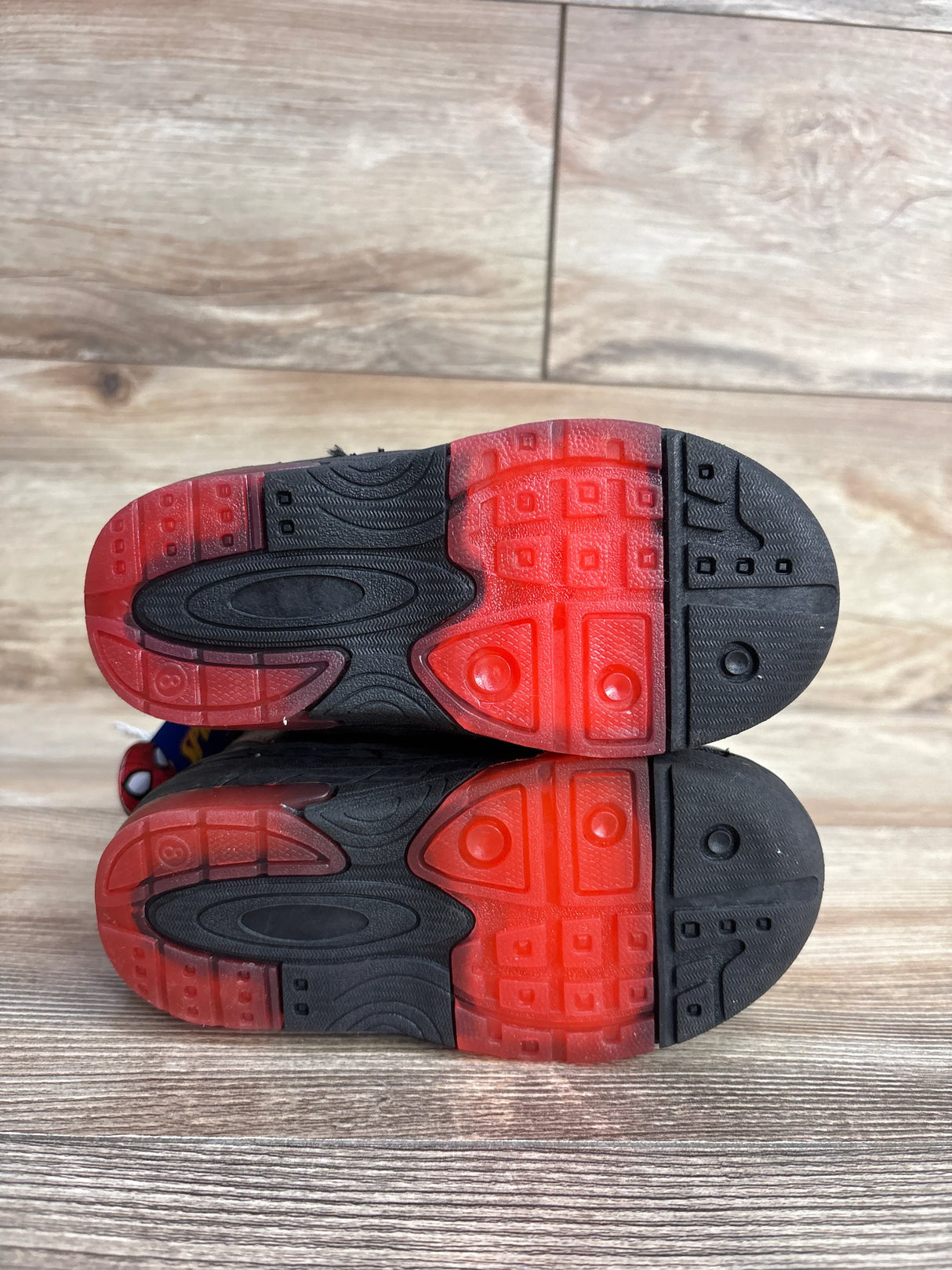 Bottom view of toddler shoes with black and red rubber soles on wooden floor