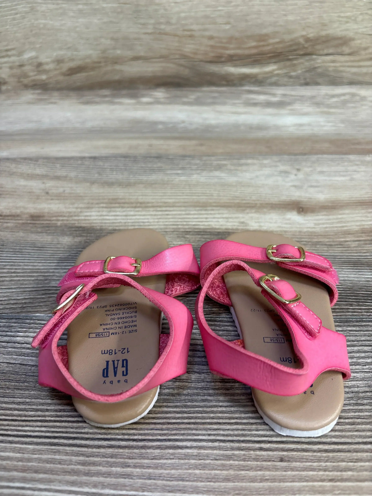 Top view of Baby Gap toddler pink buckle sandals size 12 to 18 months showing double adjustable buckles and printed insole on wood-grain background