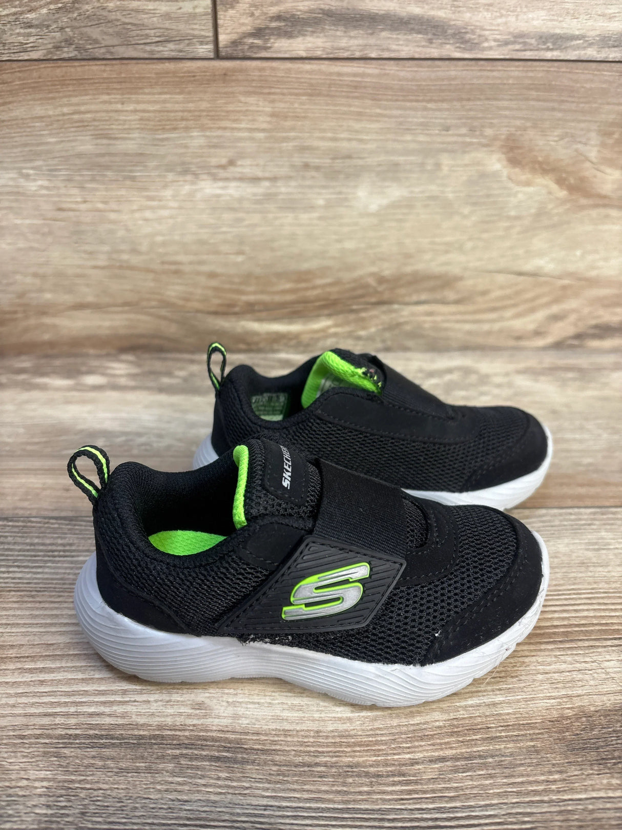Black and green Skechers toddler shoes with velcro straps on wood background