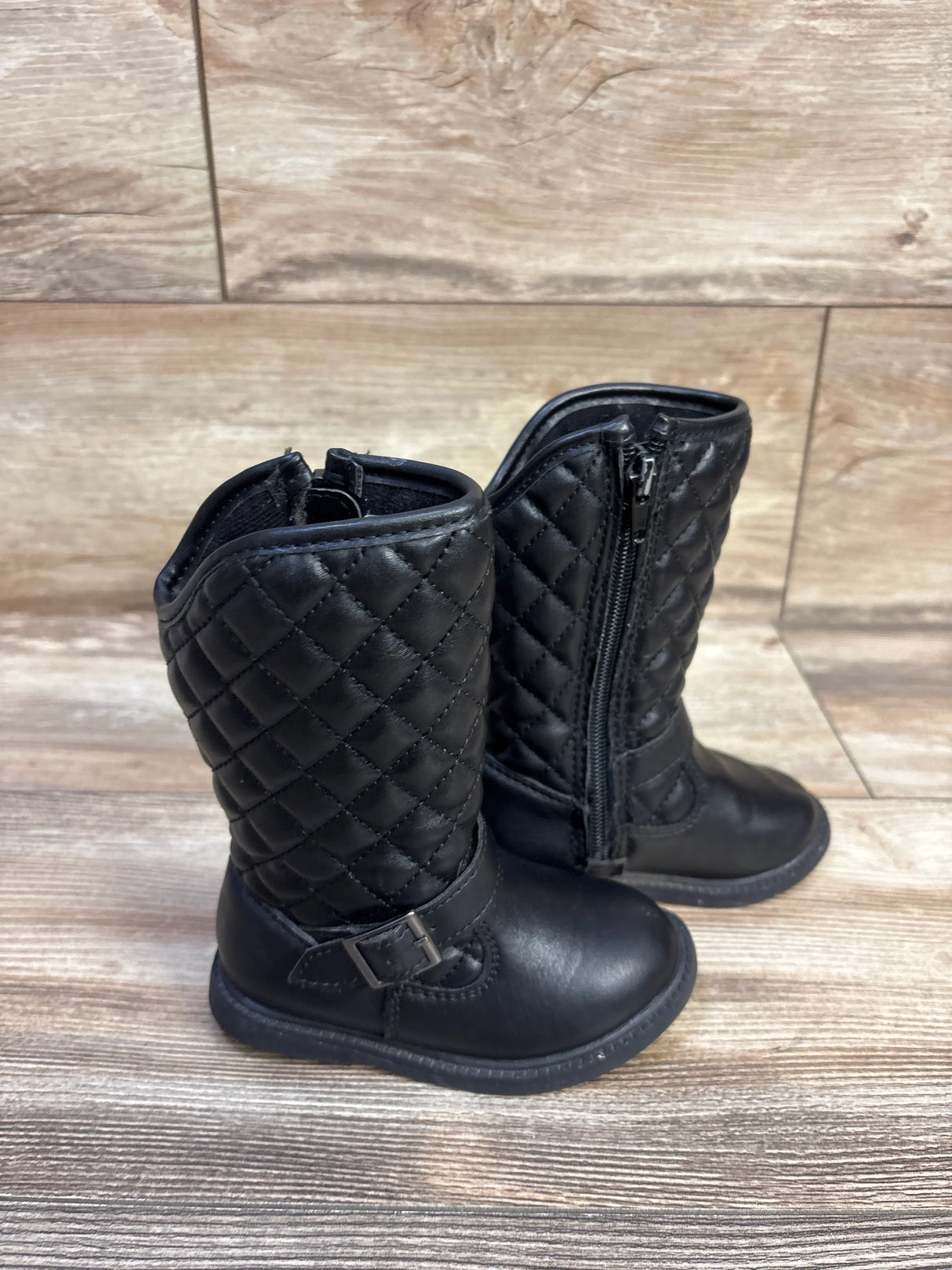Three-quarter view of toddler Carter’s quilted black riding boots with side zipper and buckle on wood background
