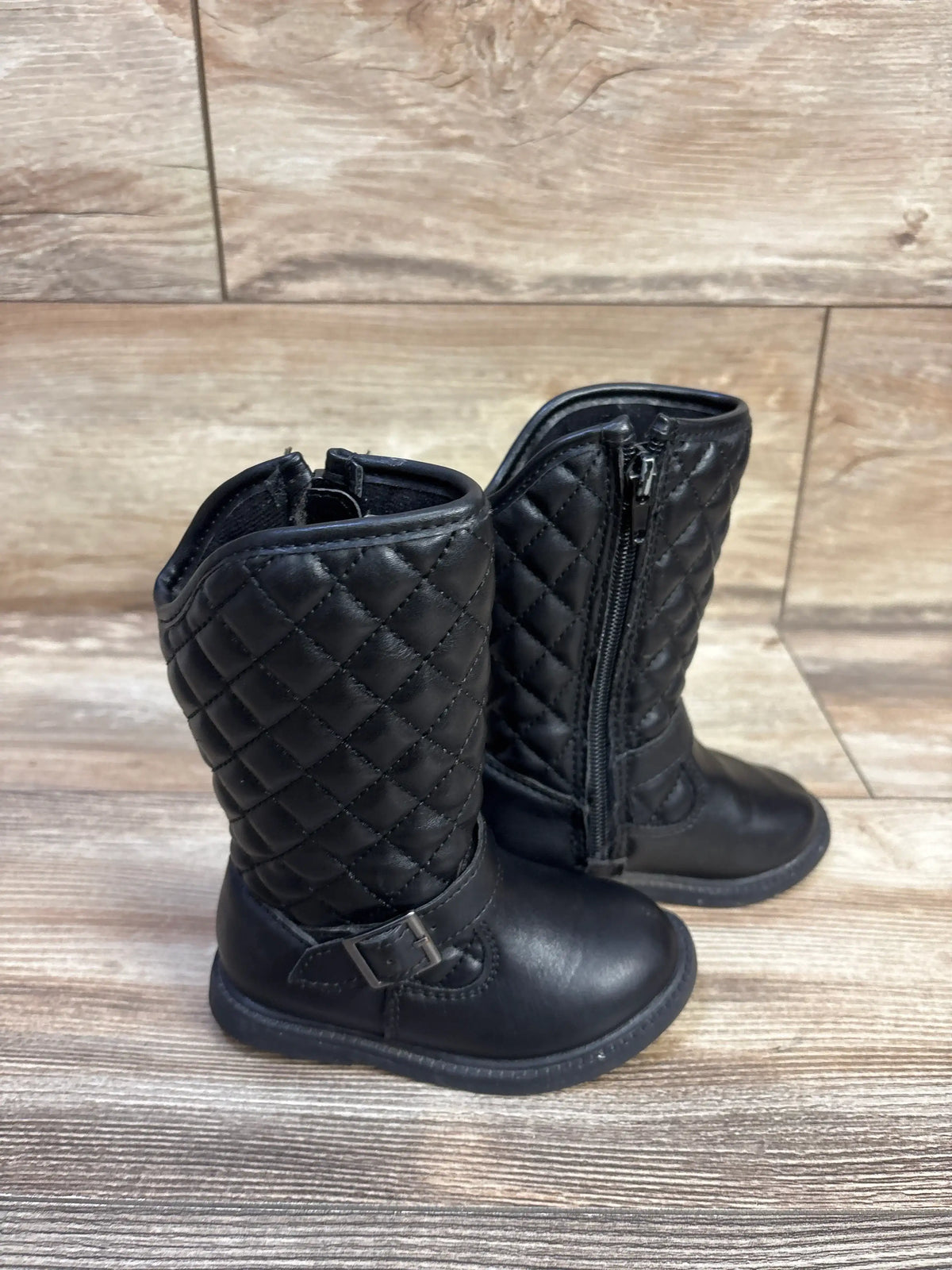 Three-quarter view of toddler Carter’s quilted black riding boots with side zipper and buckle on wood background