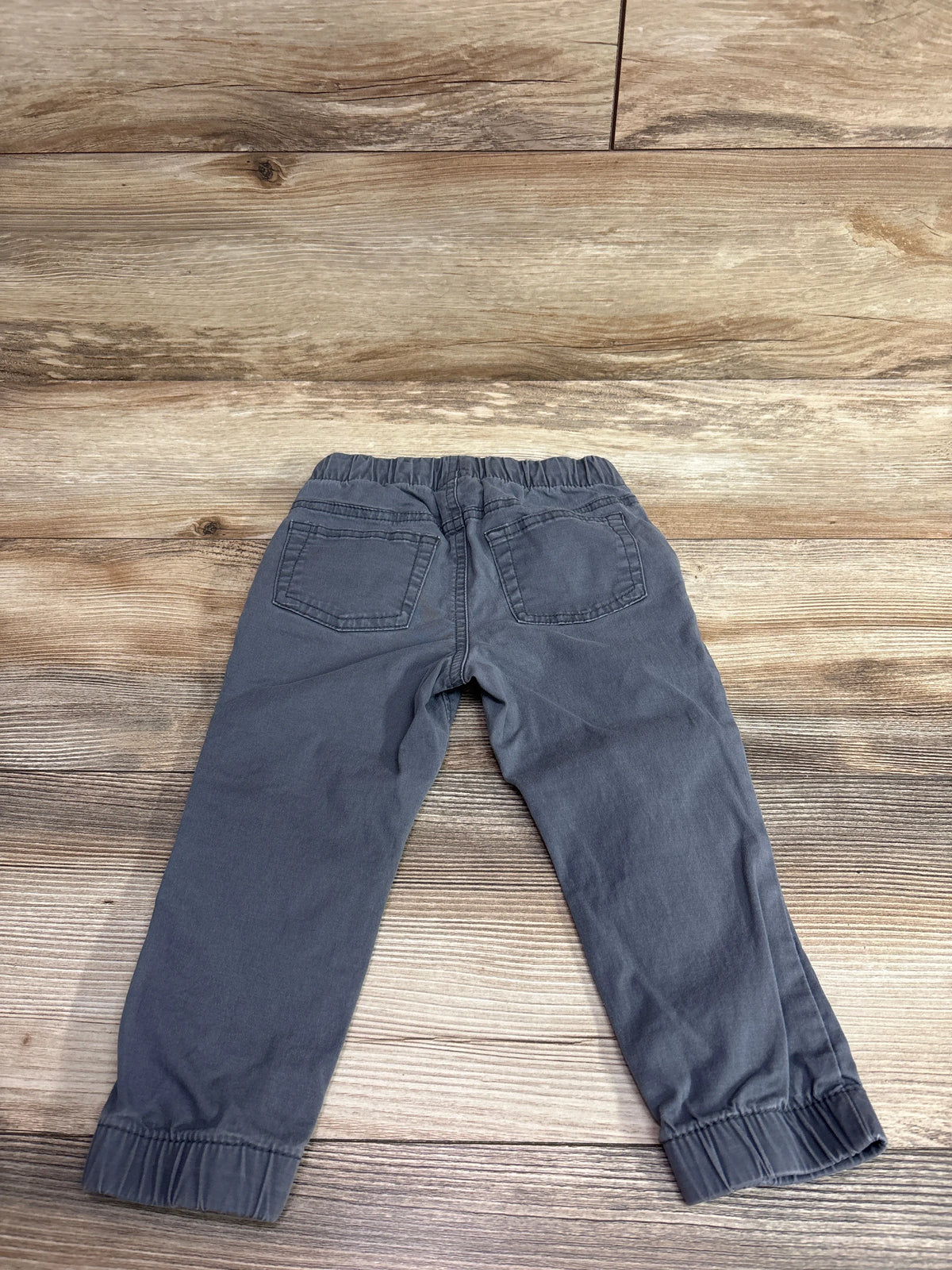 Rear view of Cat & Jack drawstring jogger pants in gray, size 2T, showcasing back pockets and elastic cuffs on a wood surface
