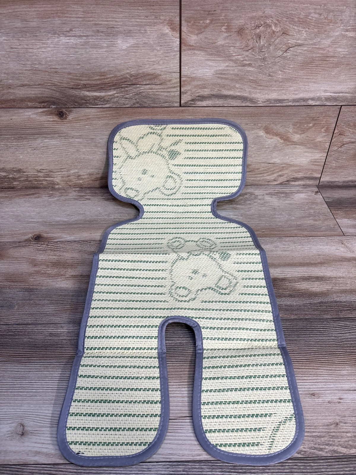 Top-down of universal stroller cool seat liner showing woven fabric, green giraffe stripes and grey trim on wood floor