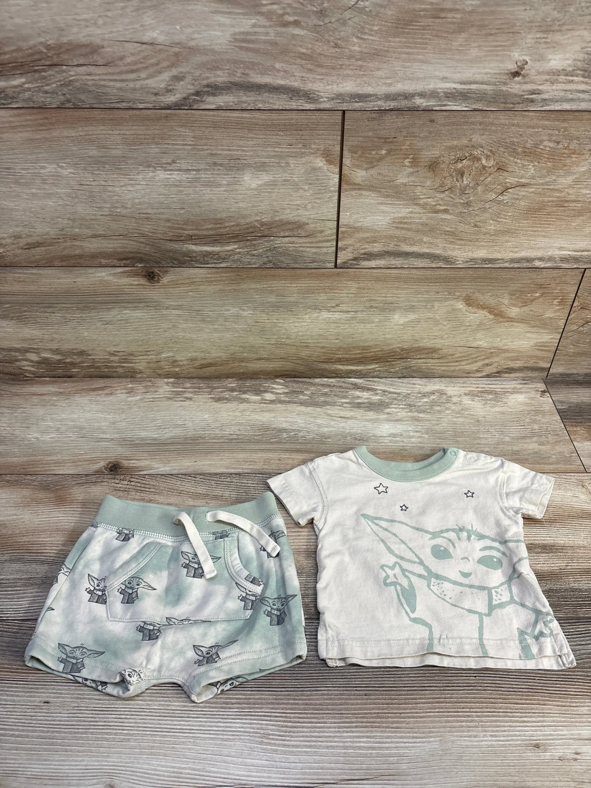 Top-down view of beige Baby Gap x Star Wars 2pc shirt and shorts set showcasing Grogu graphics and allover print on a wood floor
