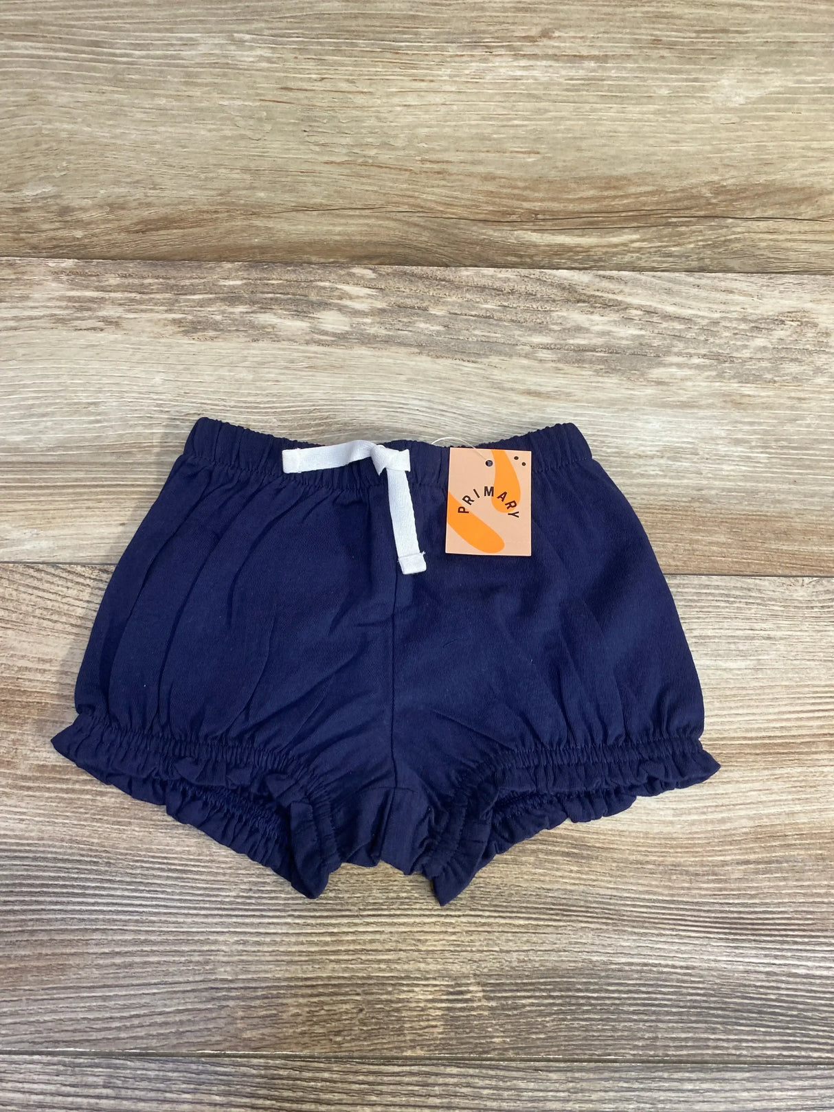 Flat lay of navy baby bloomer (3-6 months) showing elastic waistband, white drawstring, and ruffled leg openings on wood background