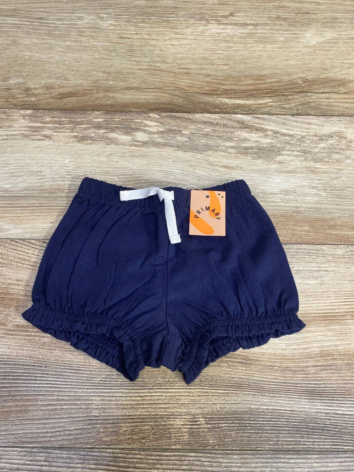 Flat lay of navy baby bloomer (3-6 months) showing elastic waistband, white drawstring, and ruffled leg openings on wood background
