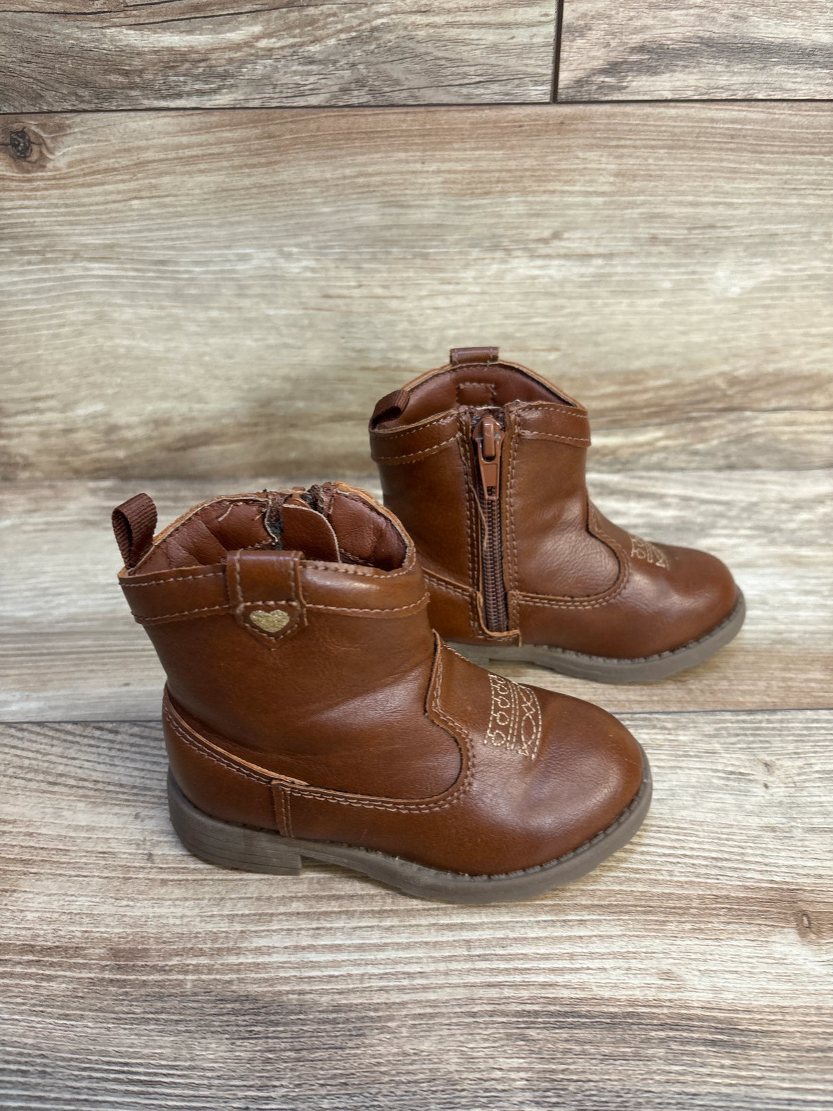 Brown leather toddler ankle boots with side zippers and heart detail on wooden floor