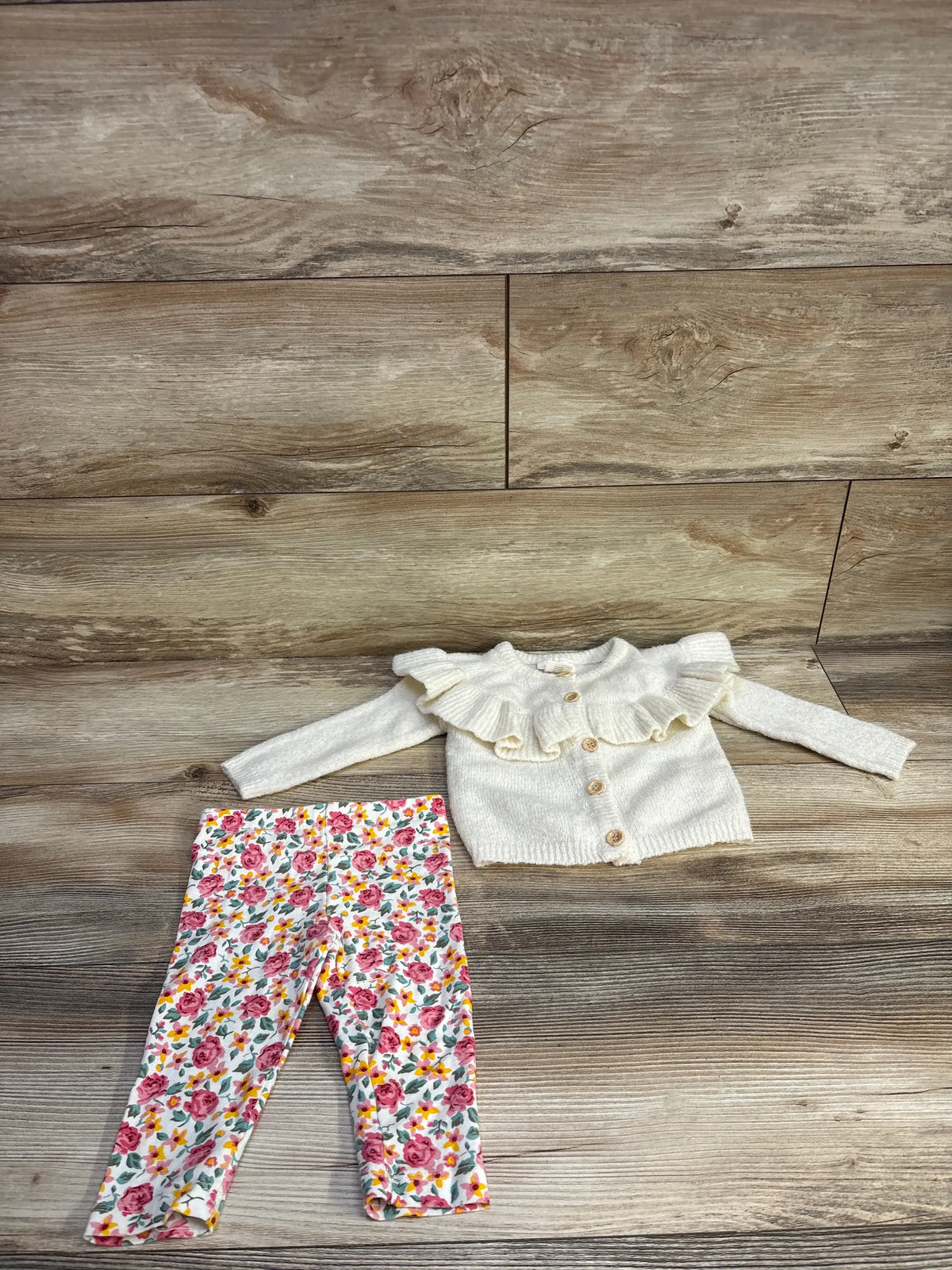 Flat lay of ivory knit ruffle cardigan with wooden buttons and floral leggings showcasing ruffle collar on wood background