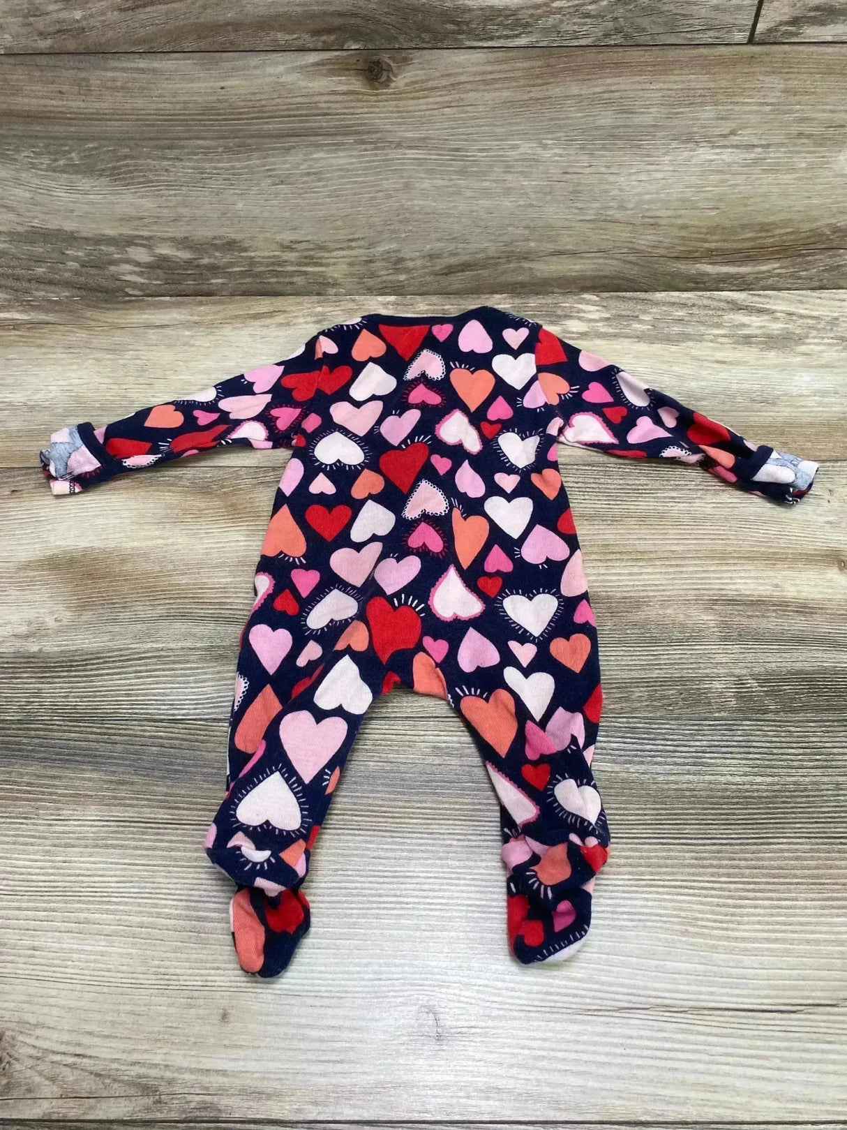 Flat lay of Old Navy footed baby sleeper (0-3M) navy with pink and red heart print, long sleeves and fold-over cuffs on wood
