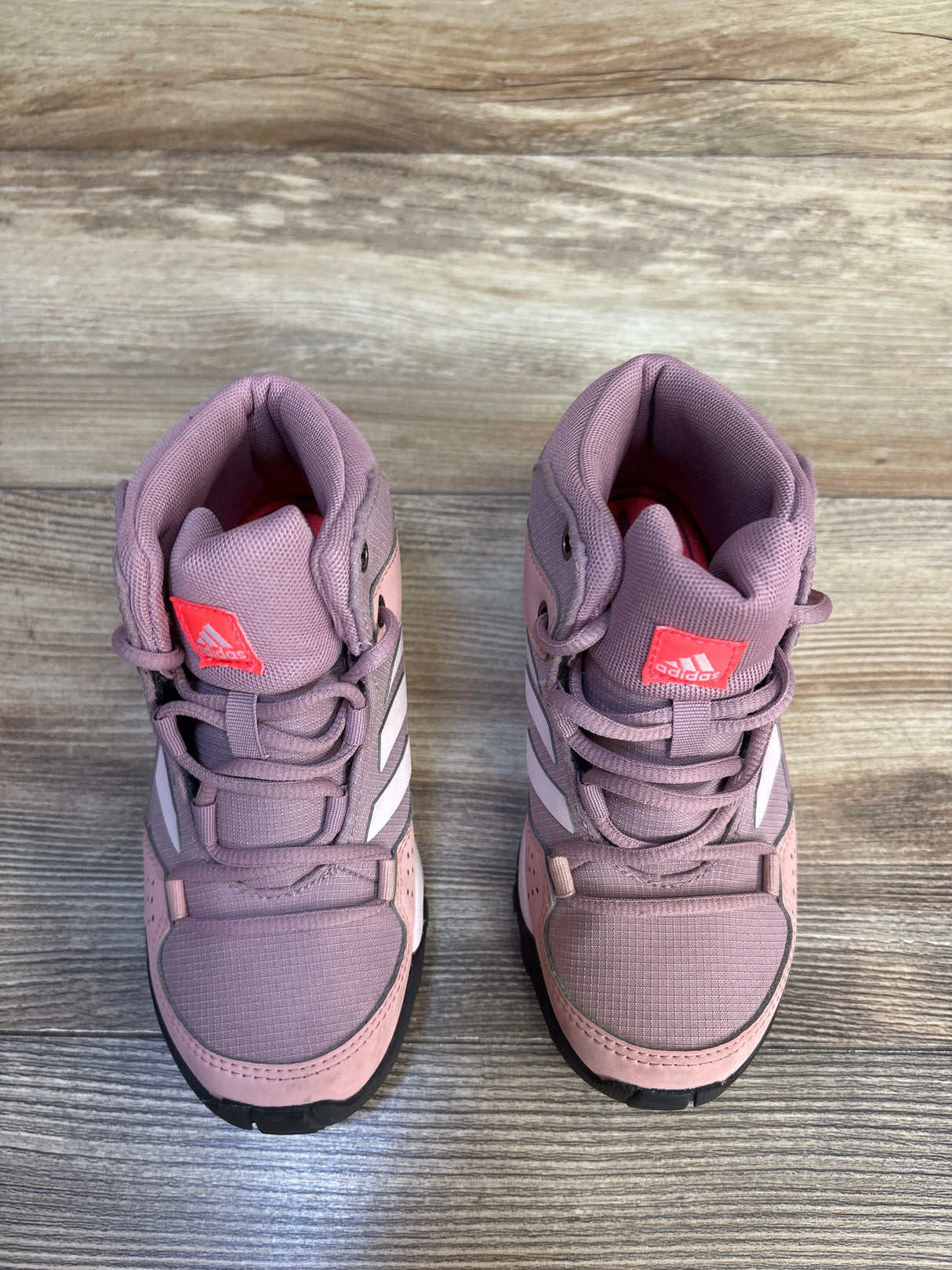 Pink Adidas kids high-top sneakers with white stripes on wood floor
