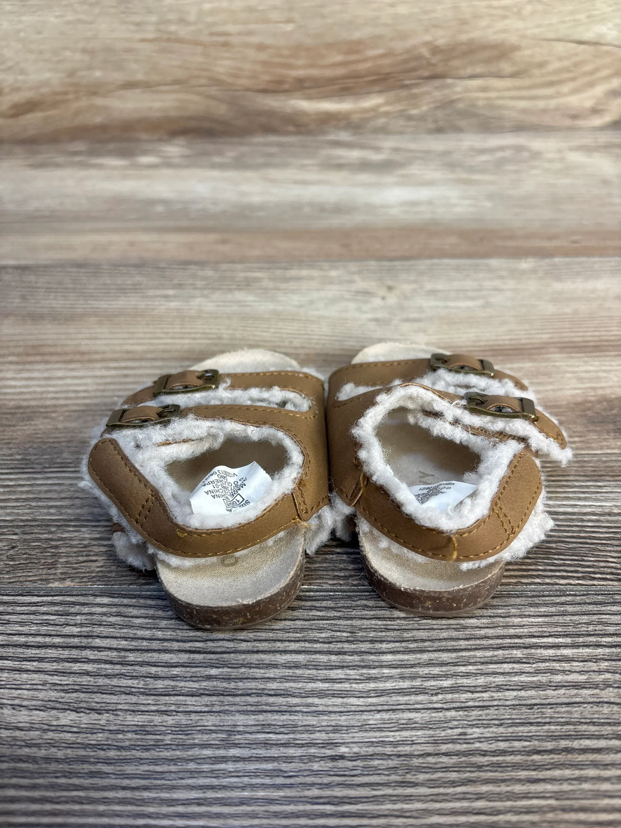 Tan toddler sandals with white fleece lining and buckles on wooden background