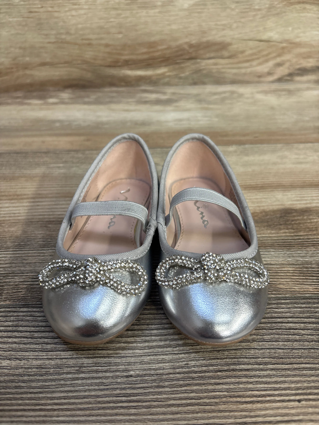 Silver girls' dress shoes with rhinestone bows on wooden floor